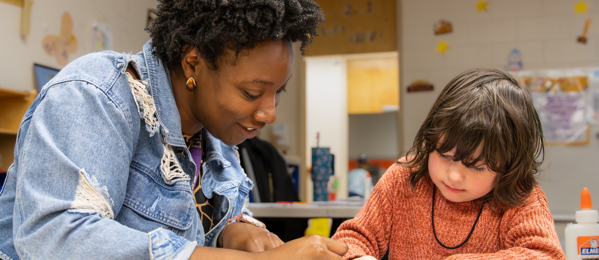 Teacher leans over and colors a worksheet with a student