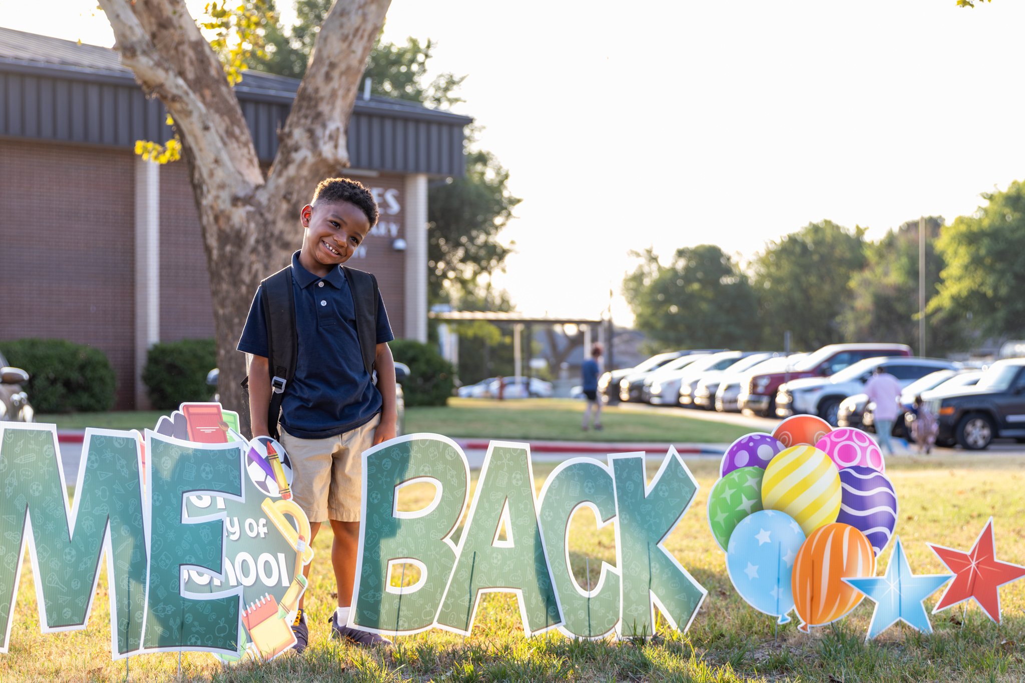 A student smiles and poses next to a "Welcome Back" sign