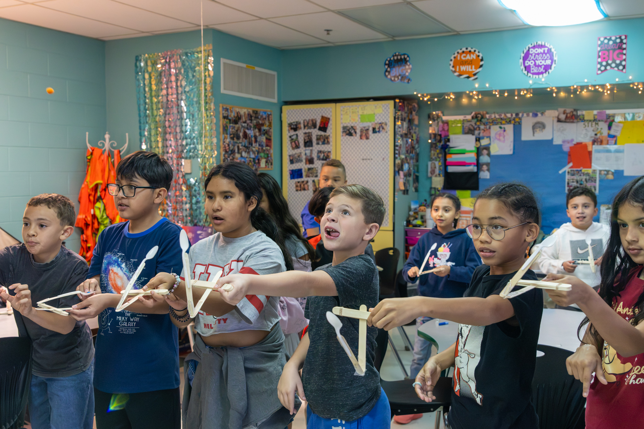 Students stand in a line, launching soft pom poms from their constructed catapults