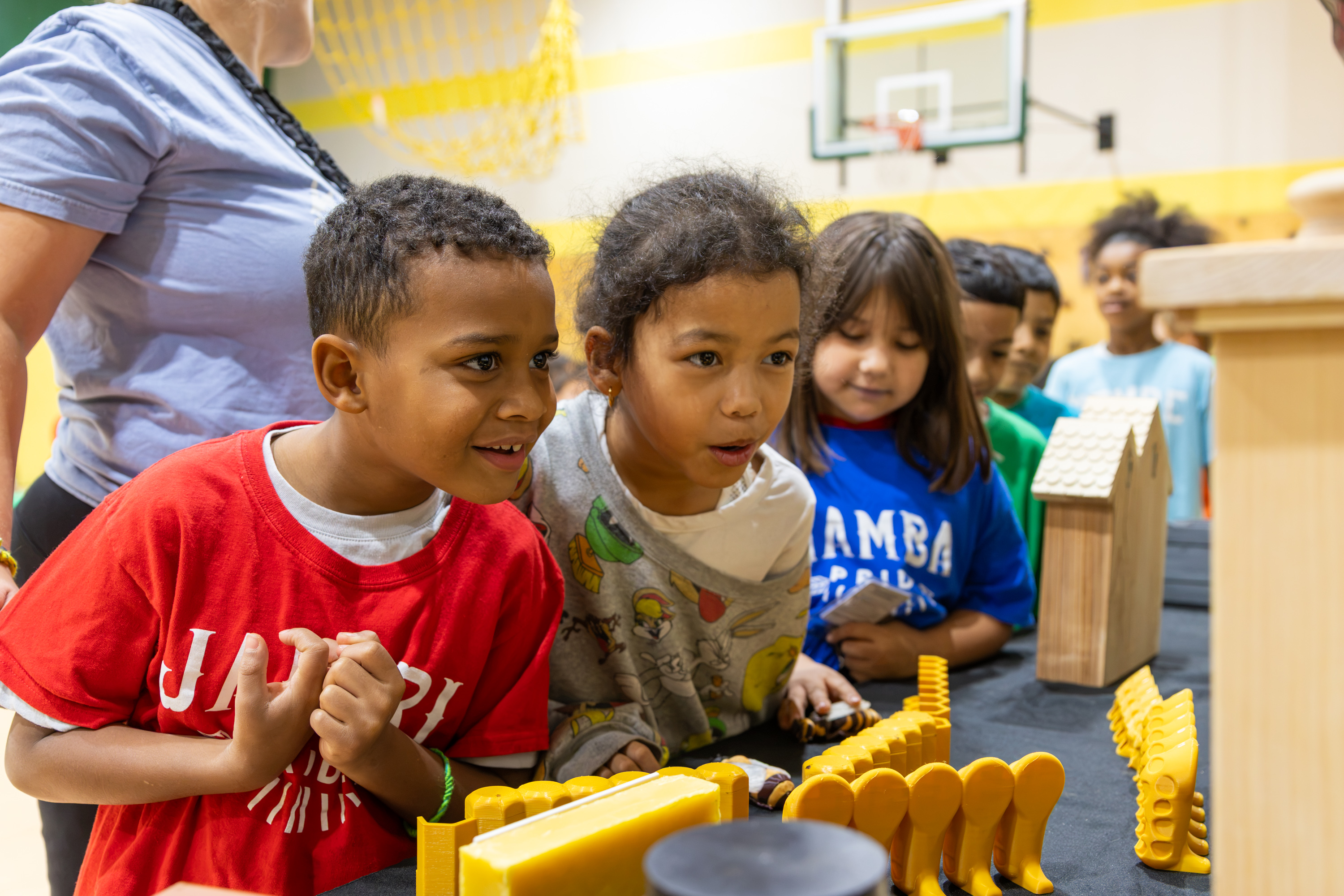 A group of young students look intently at honeycomb samples and bee models arranged on a presentation table.