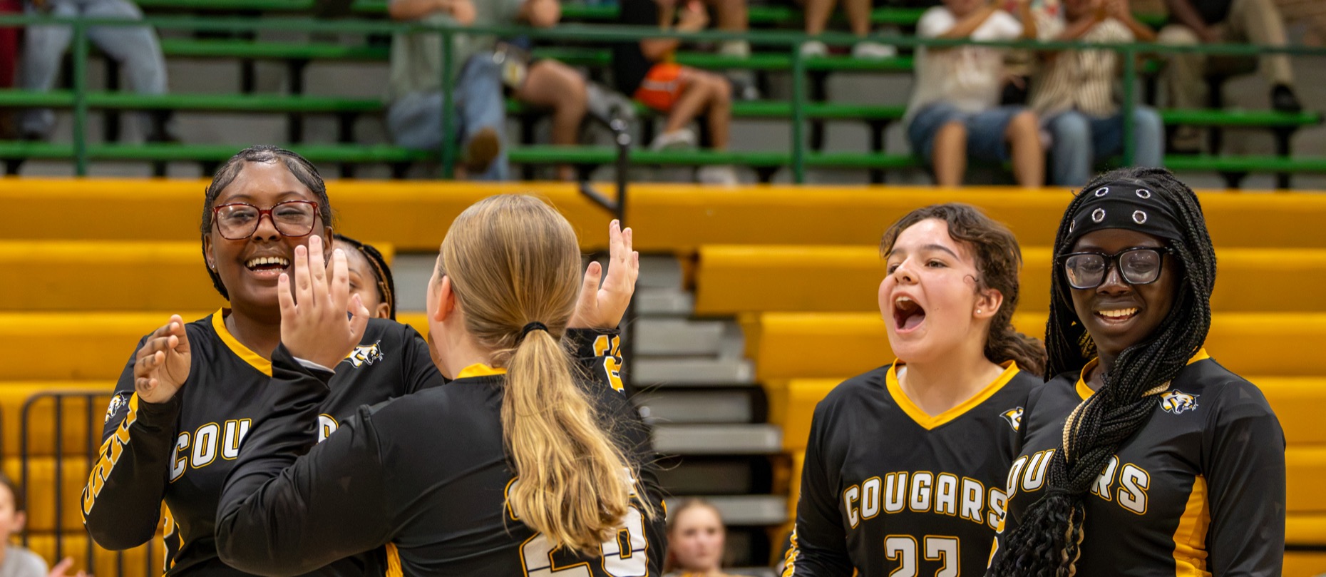 Cooper Middle School volleyball players celebrate together on the court, smiling and raising their hands after a point.