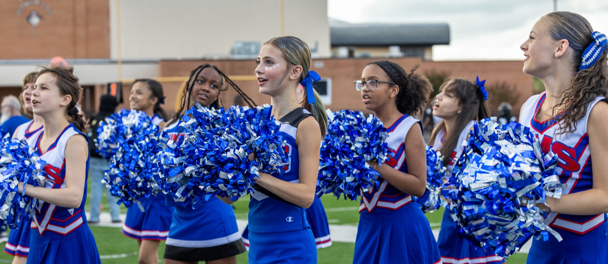 Hefner cheerleaders clap their pom poms together on the sideline of a football game