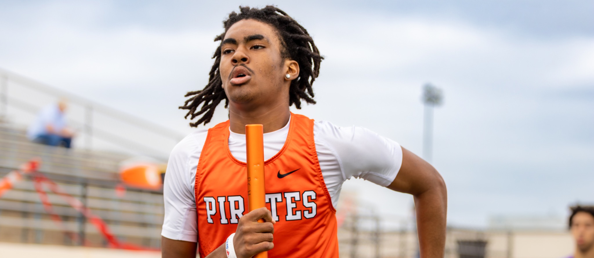 Track athlete in orange uniform runs while holding a relay baton