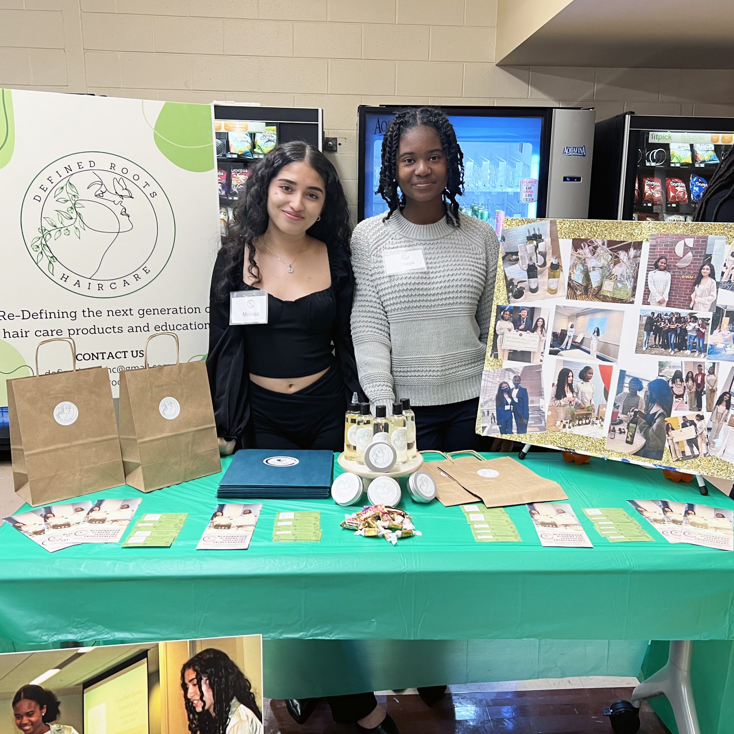 Two female students at a career fair show off their ideas at their table with signs and products.