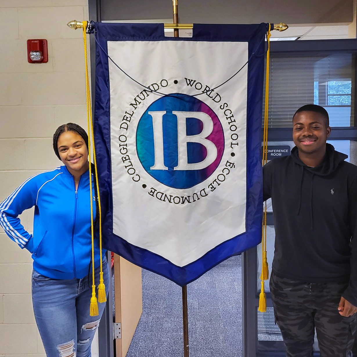 Two students standing next to an IB flag on a display stand