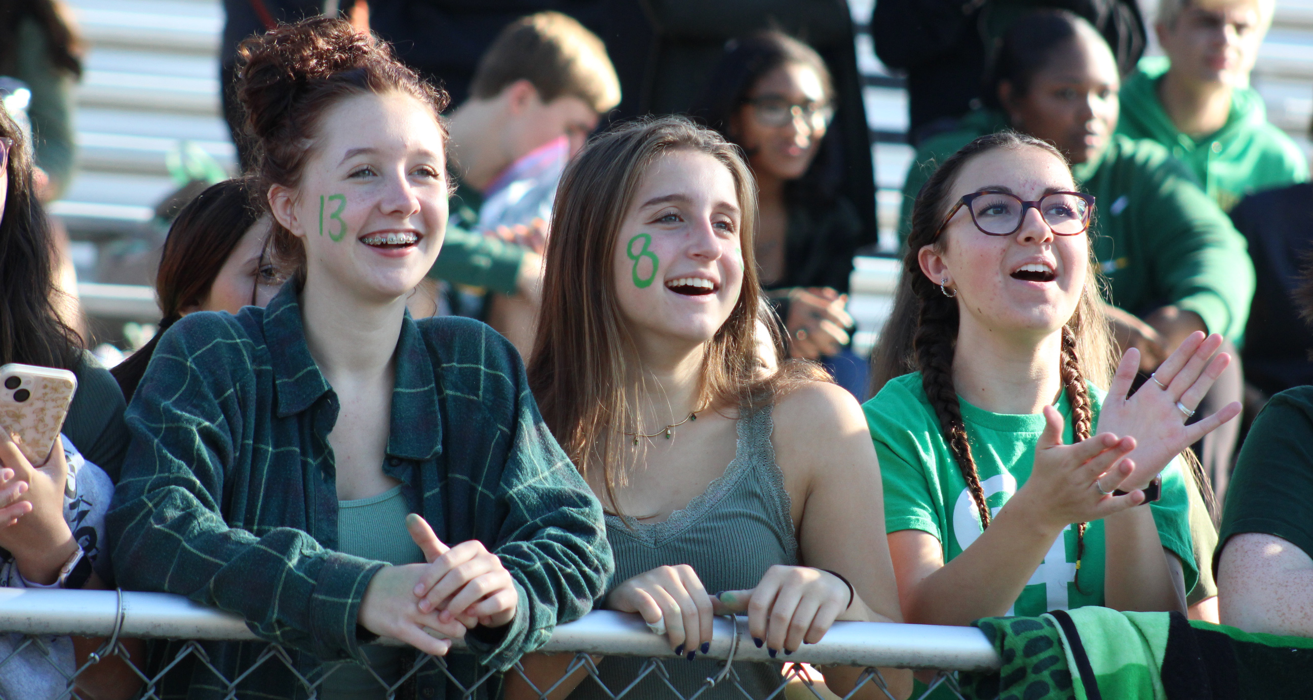 Three girls watching a football game on the stadium bleachers