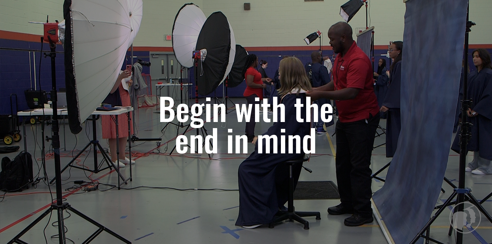 A photographer is helping a student adjust her gown before a photo