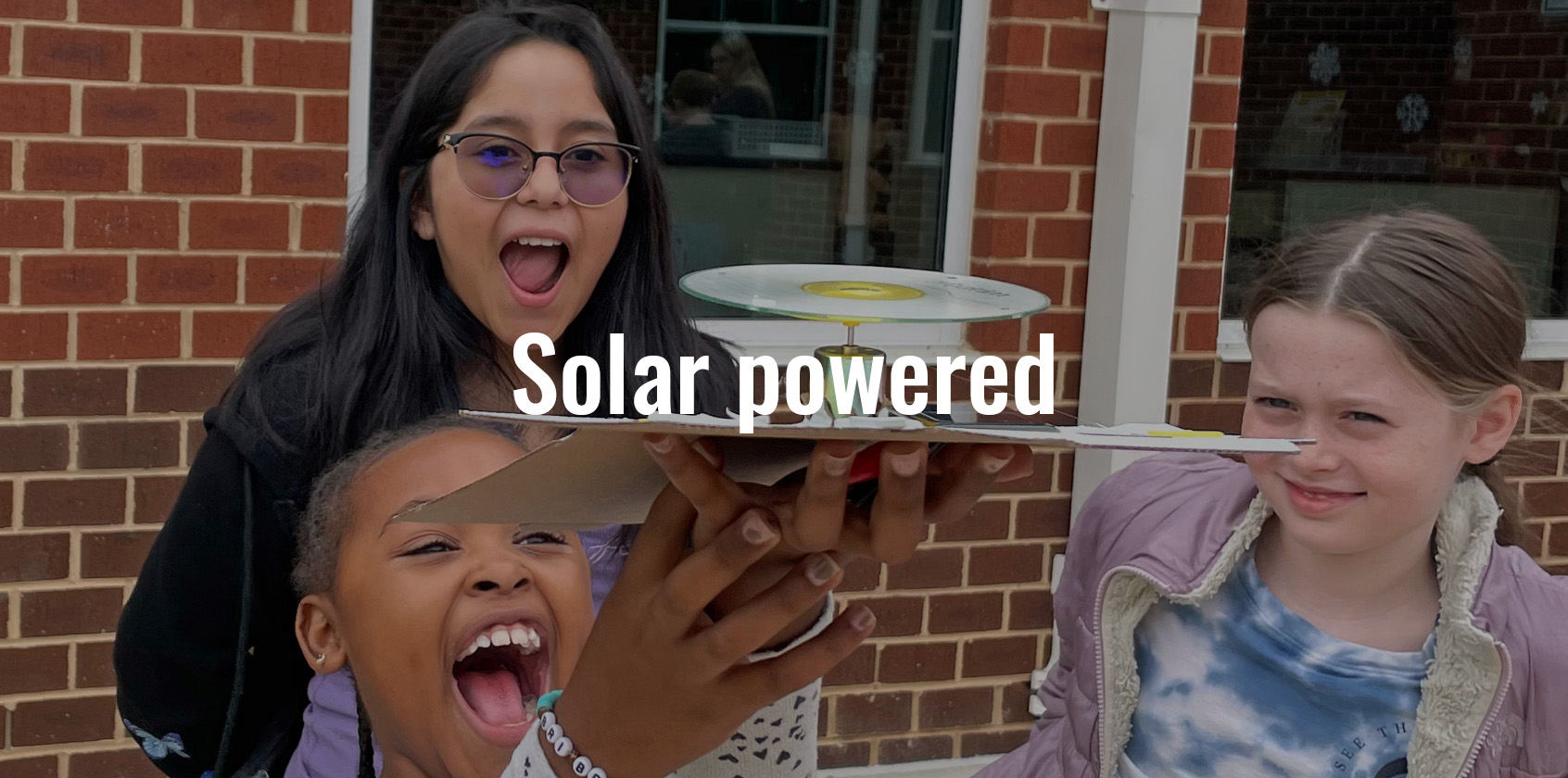 Three students are excited to watch a solar powered whirligig in action
