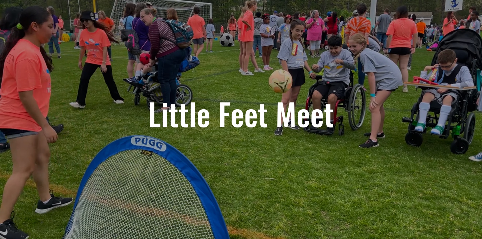 Three students help and guide a student in a wheelchair throw a soccer ball in a small goal