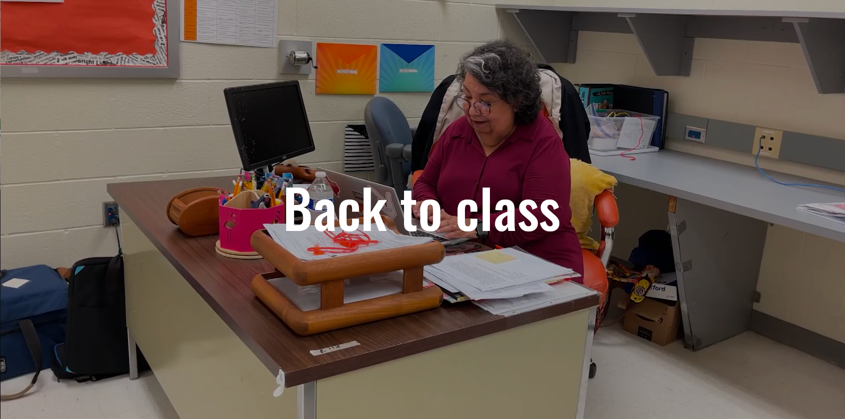 Teacher is sitting at her desk typing on her laptop