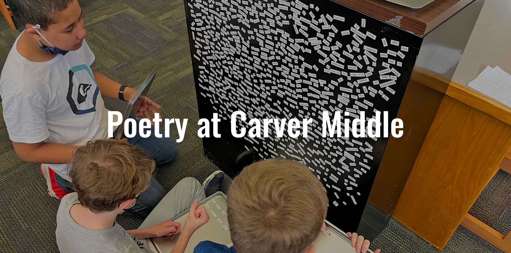 Three male students on floor looking at word magnets to put together a poem.