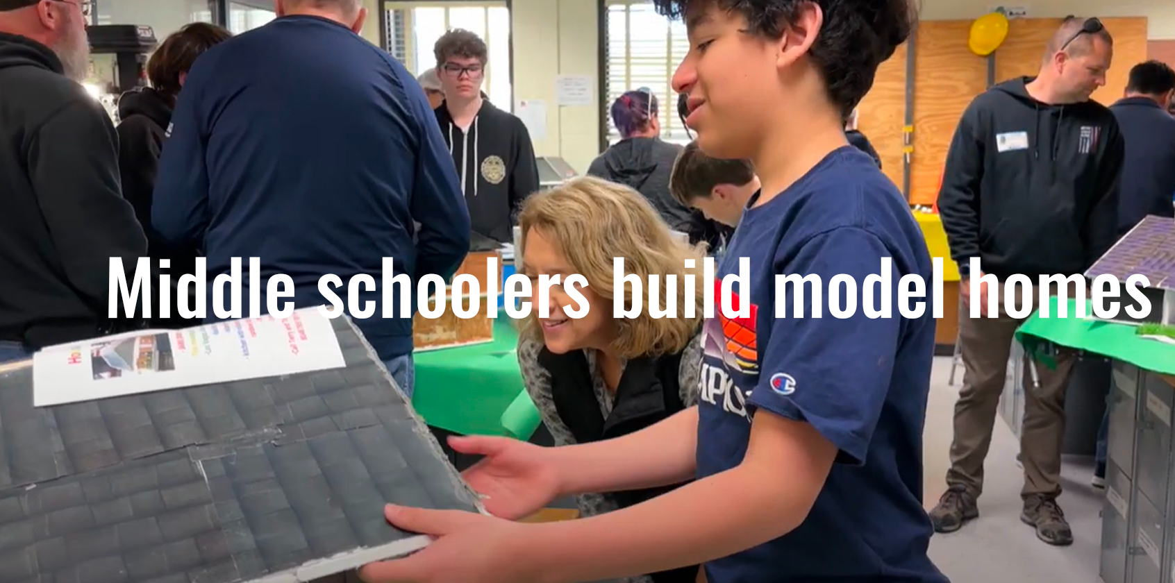 Student shows adult a home he built with craft items