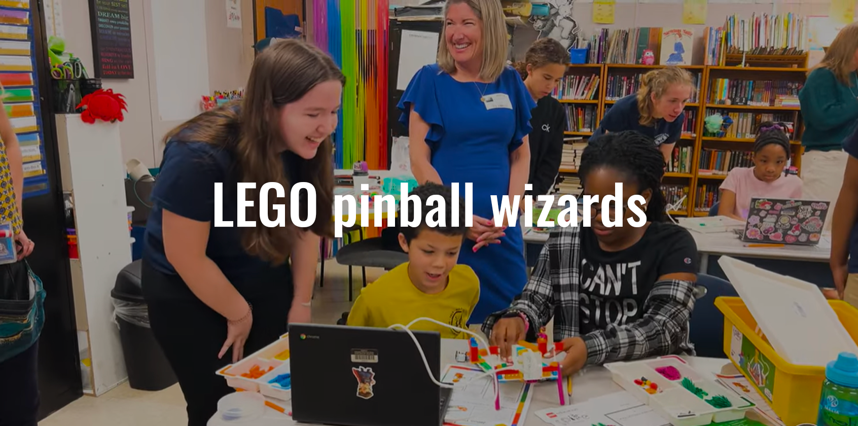 A high school student helping two younger students with a LEGO project
