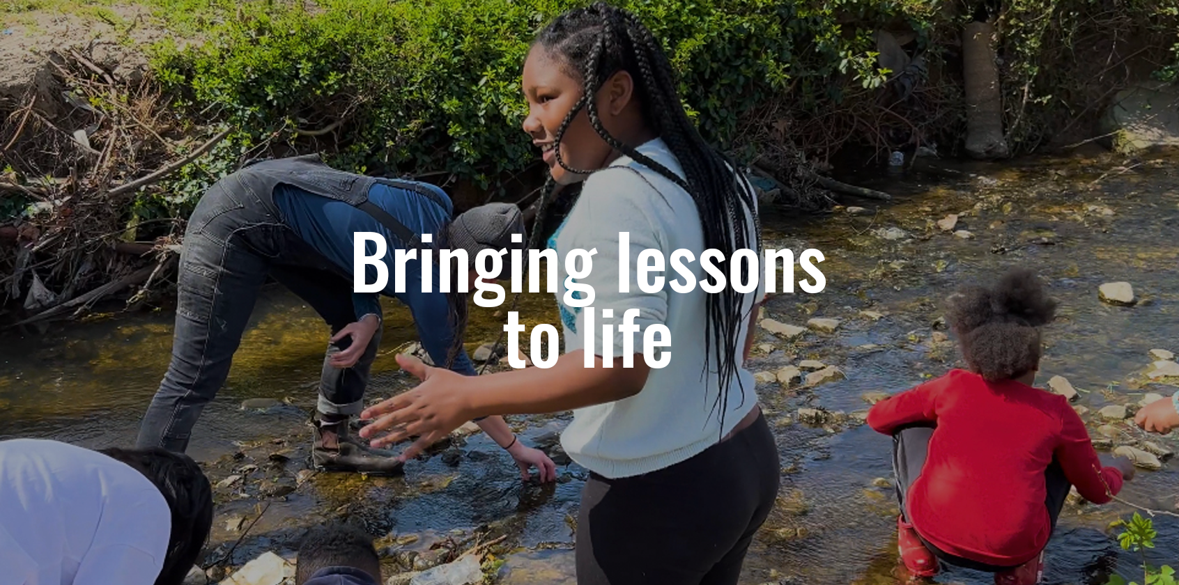 Students picking up rocks in a river with text that says "Bringing lessons to life"
