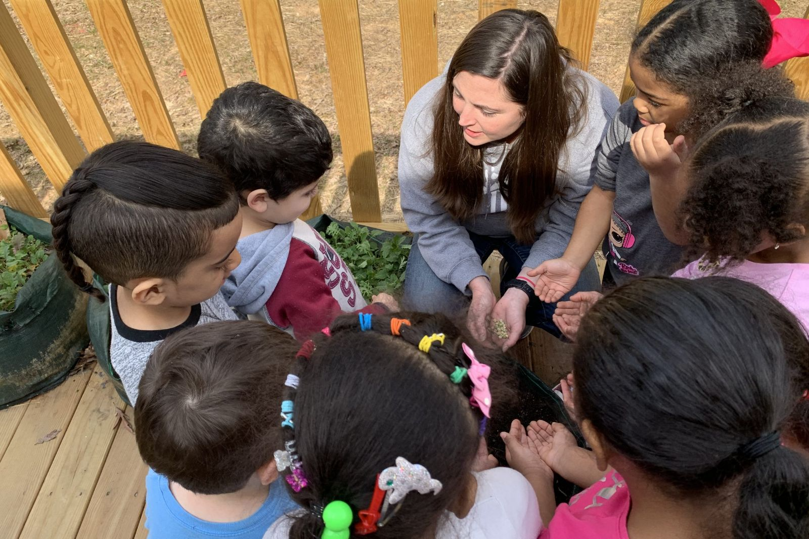 Crouched teacher talking to a circle of young students outdoors