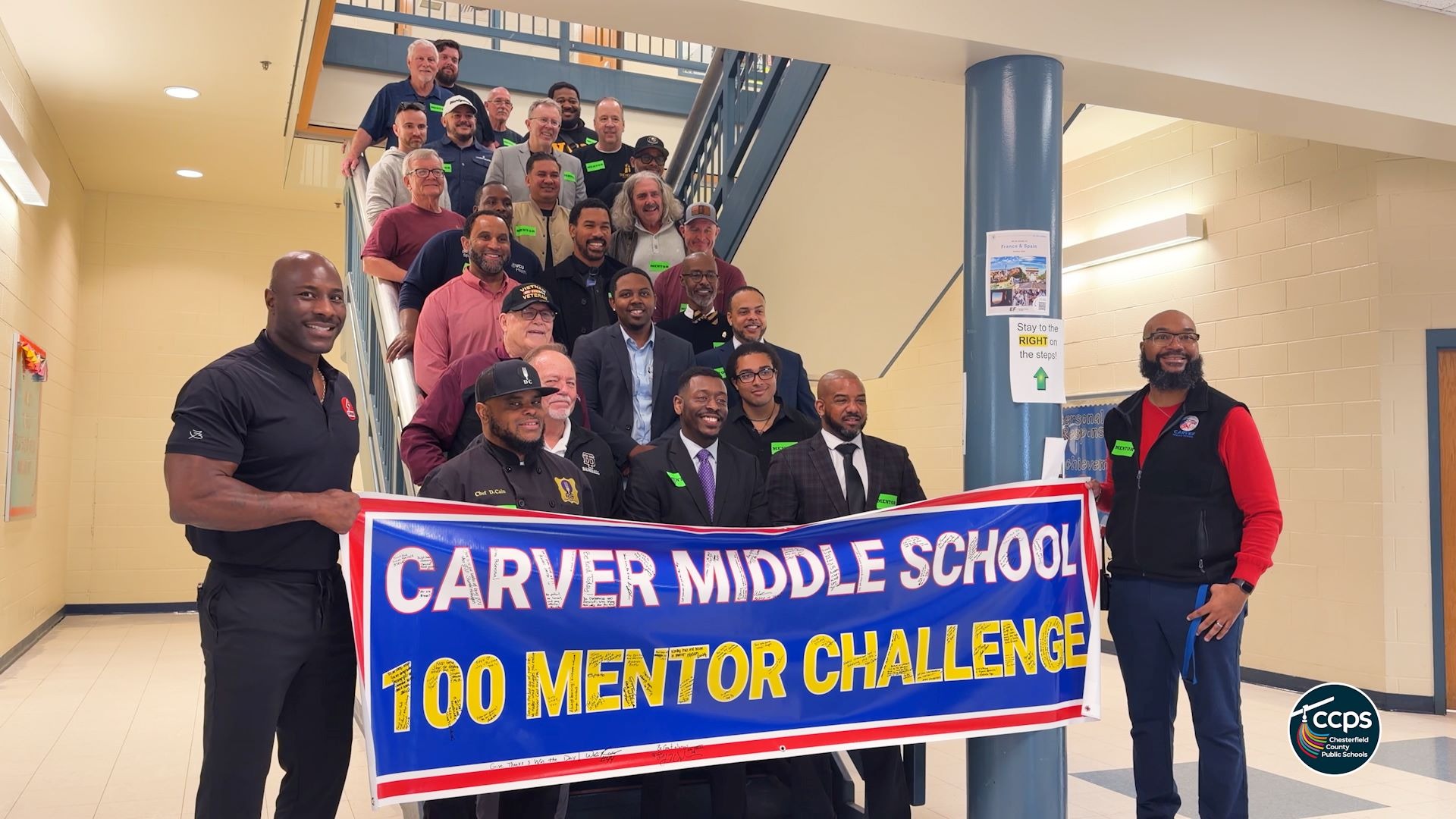 Adults standing with a banner that says "Carver Middle School 100 Mentor Challenge)
