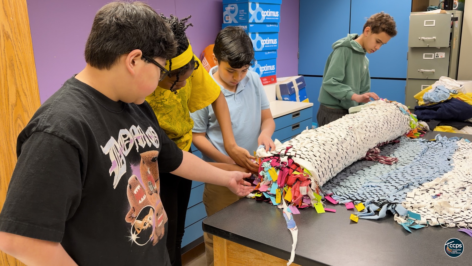 Students unrolling a large, colorful woven art piece