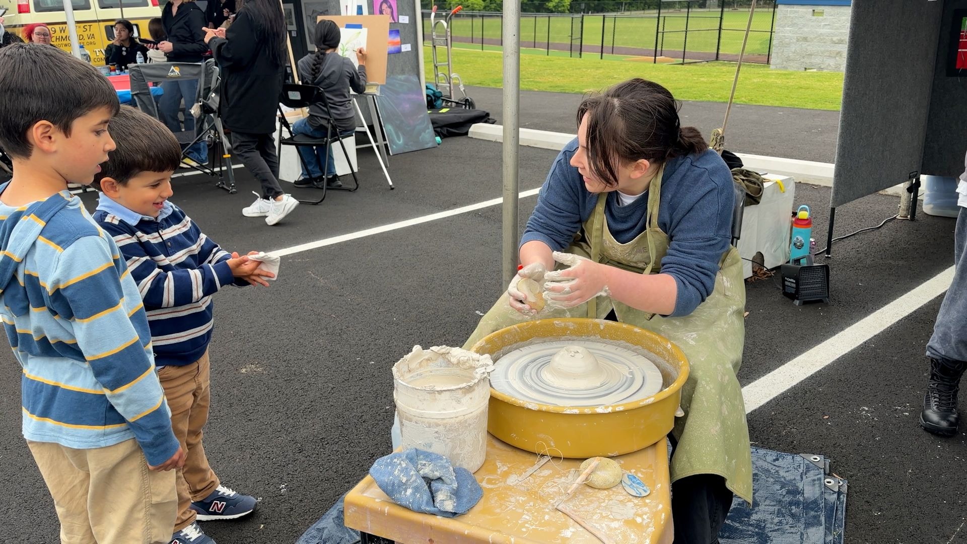Two children interacting with an older student working on a pottery wheel