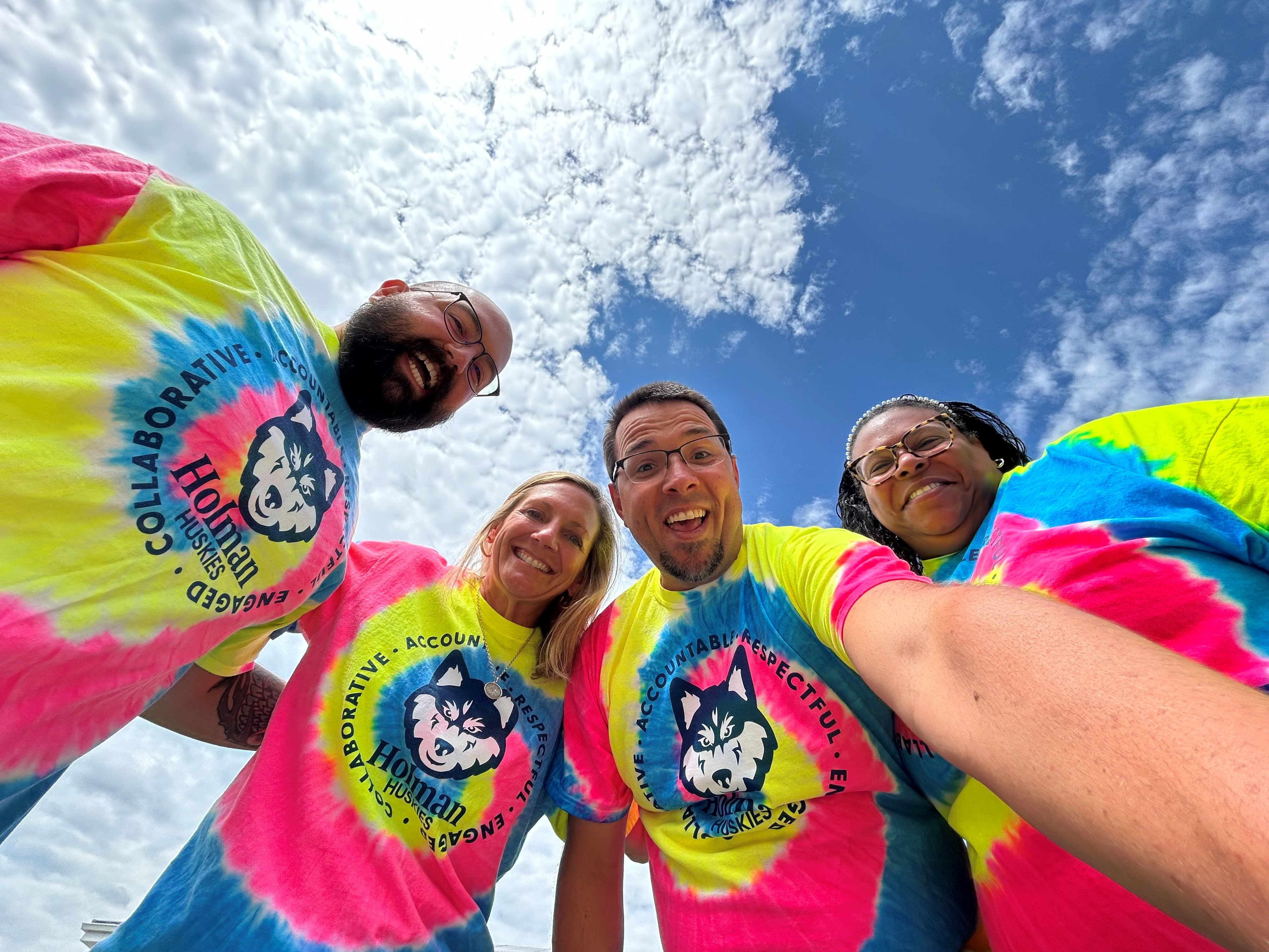a picture of Jon Meister, Susan Proffitt, Matt Baedke, and Christie Forrest smiling and wearing tie-dyed t-shirts