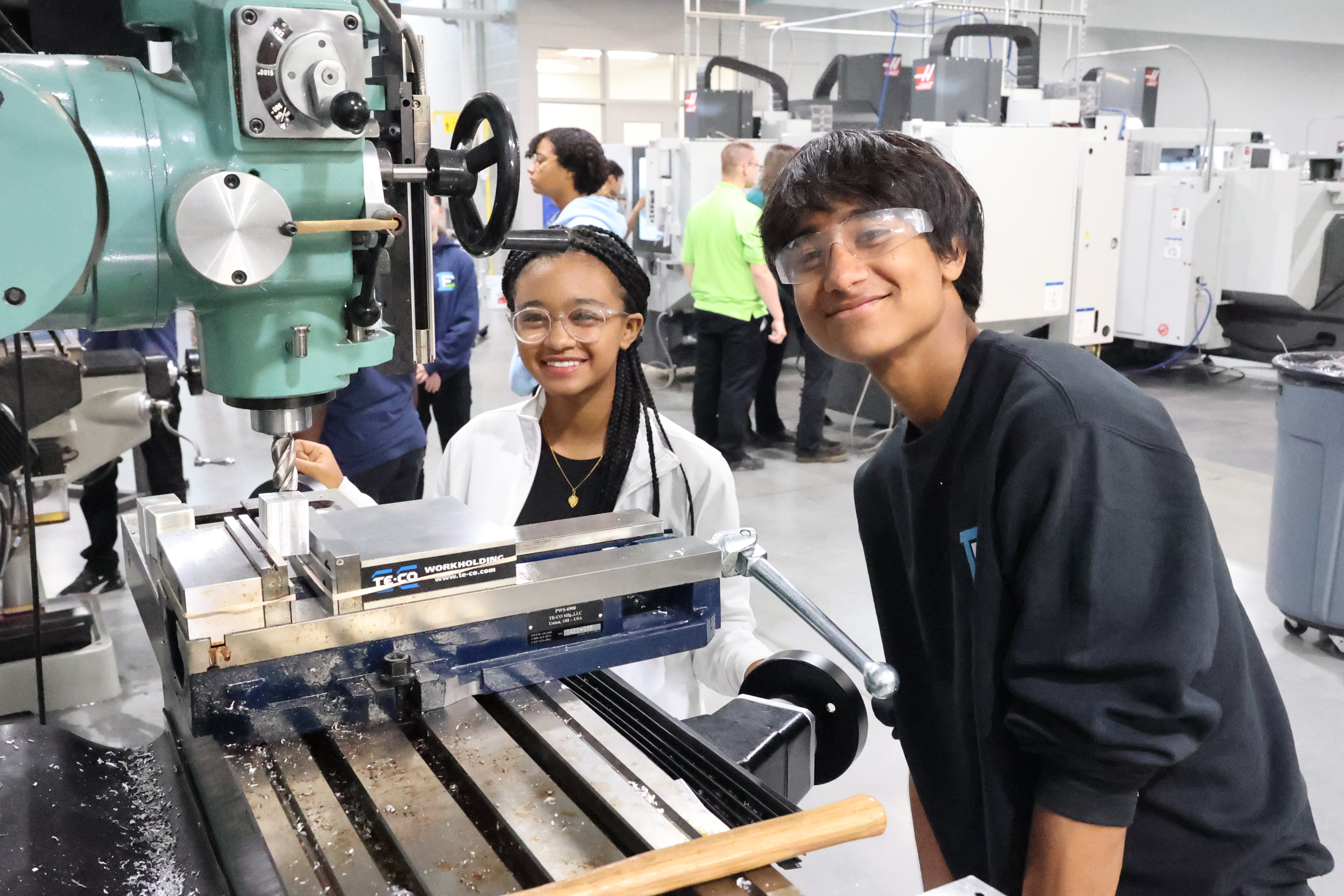 A male and female student, both of color, gather around a piece of machinery in their Pre-Engineering lab.