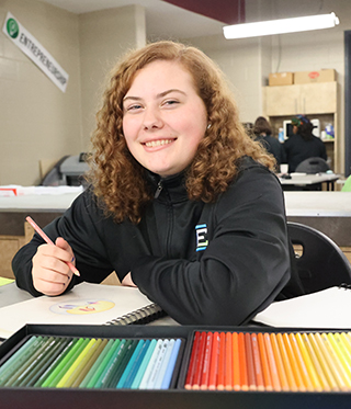 A White, female student is drawing using colored pencils as part of her Graphic Design class.