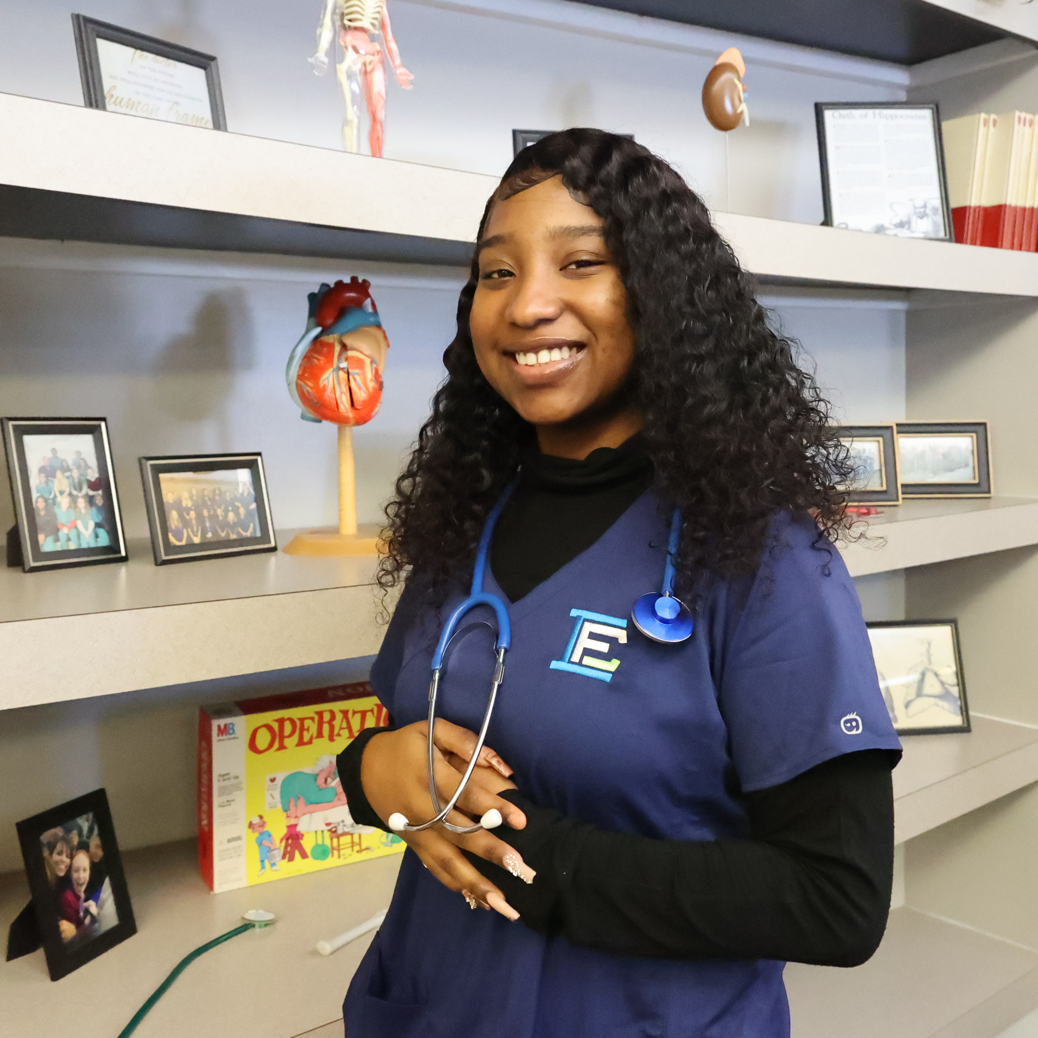 A Black, female student poses in uniform with a stethoscope around her neck in her Medical Office lab.