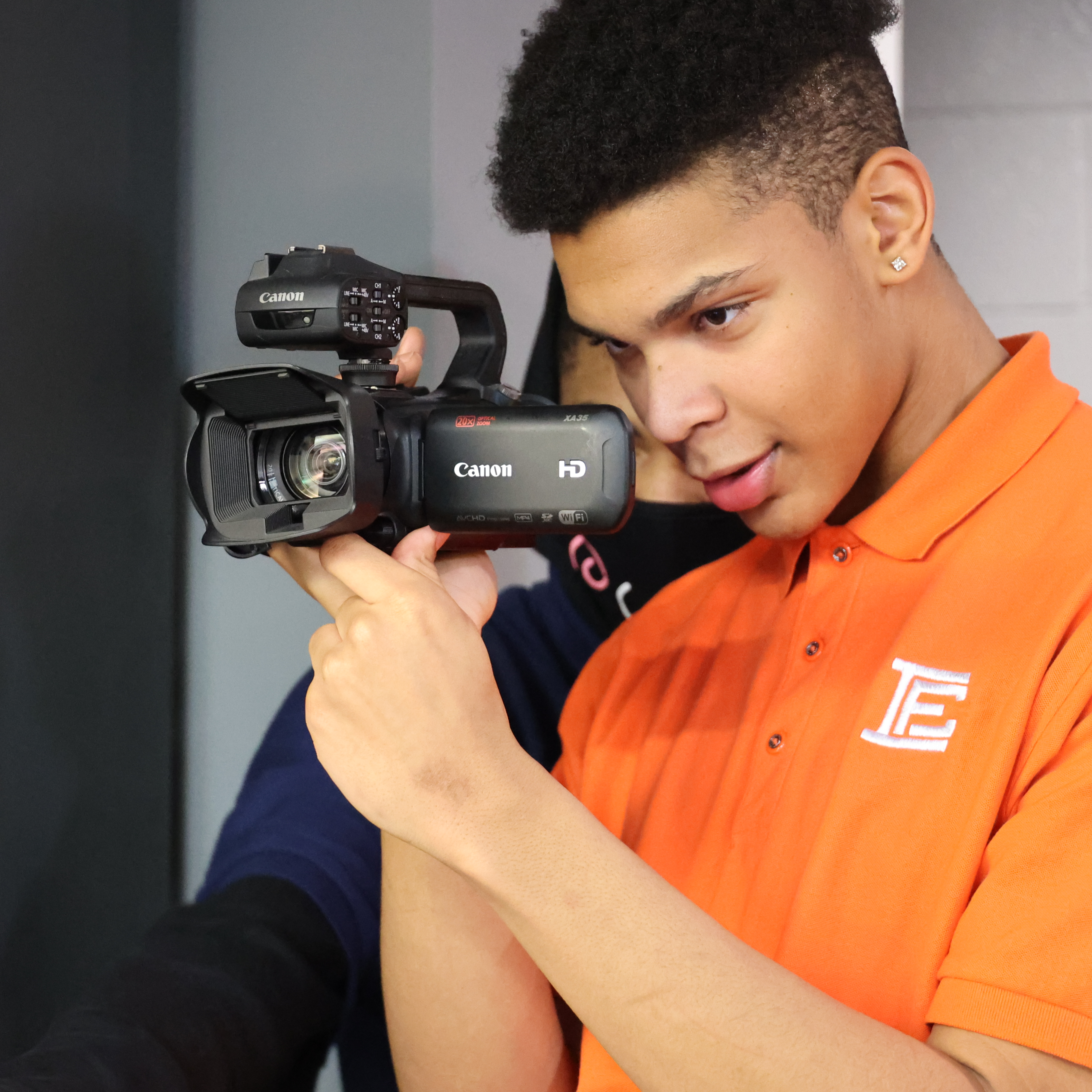 A male, Black student student holds a video camera while trying to capture a scene.
