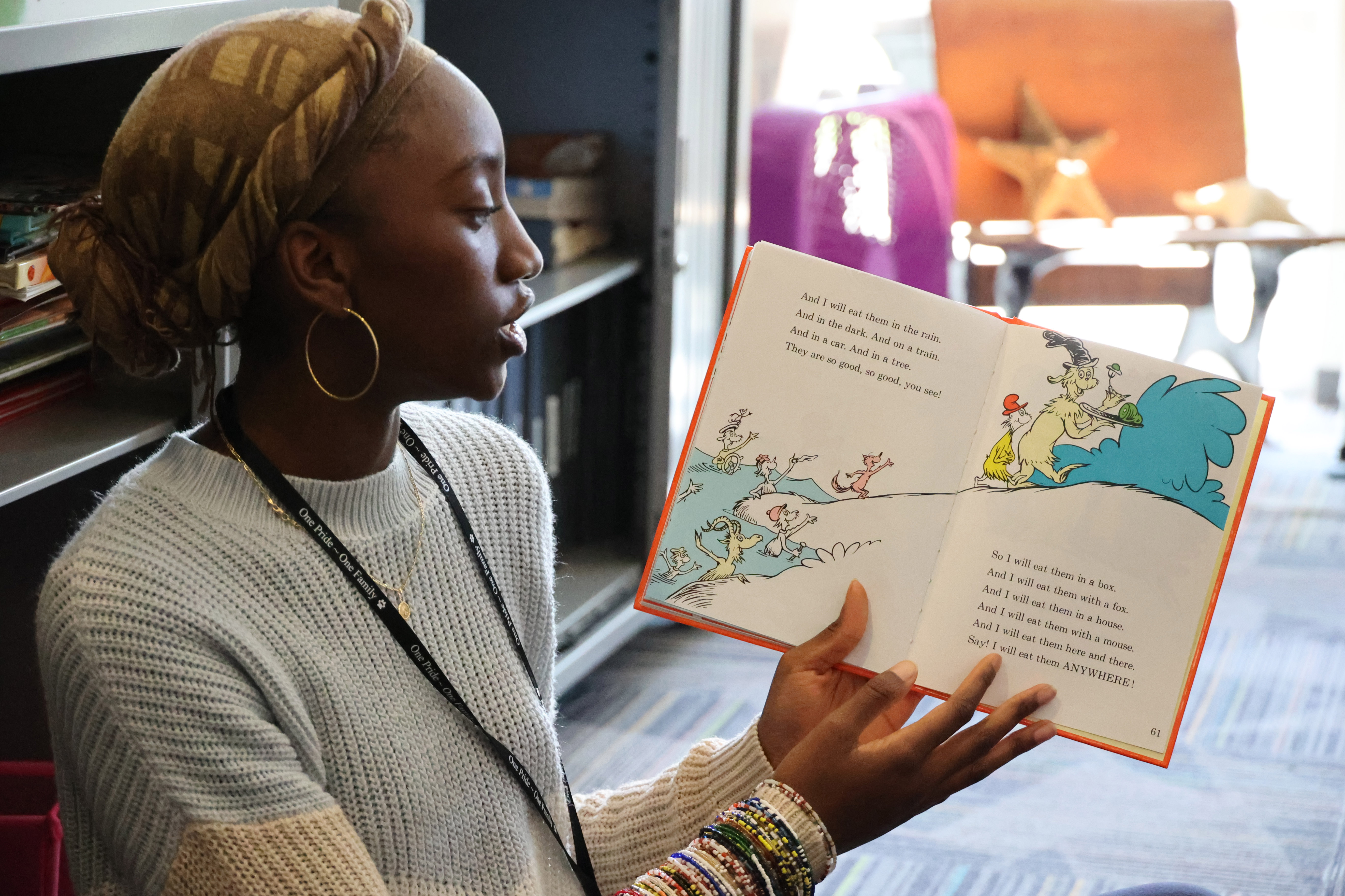 A Black, female student opens a Dr. Seuss book and begins reading to students around her.