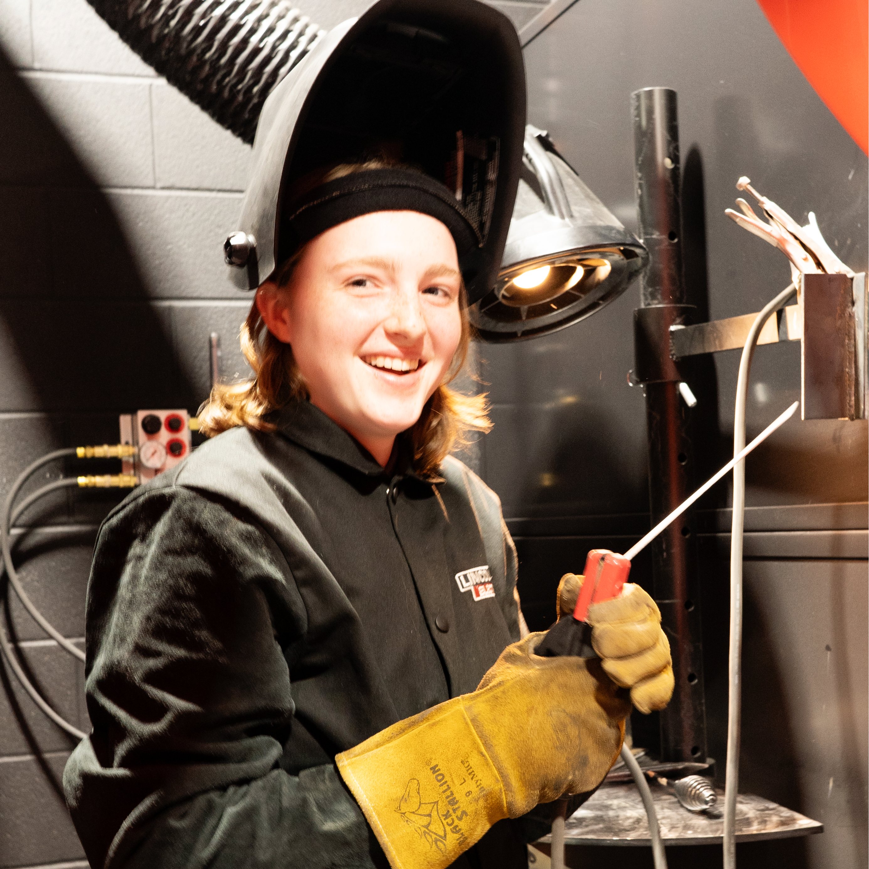 A White, female student prepares to begin welding in her booth.