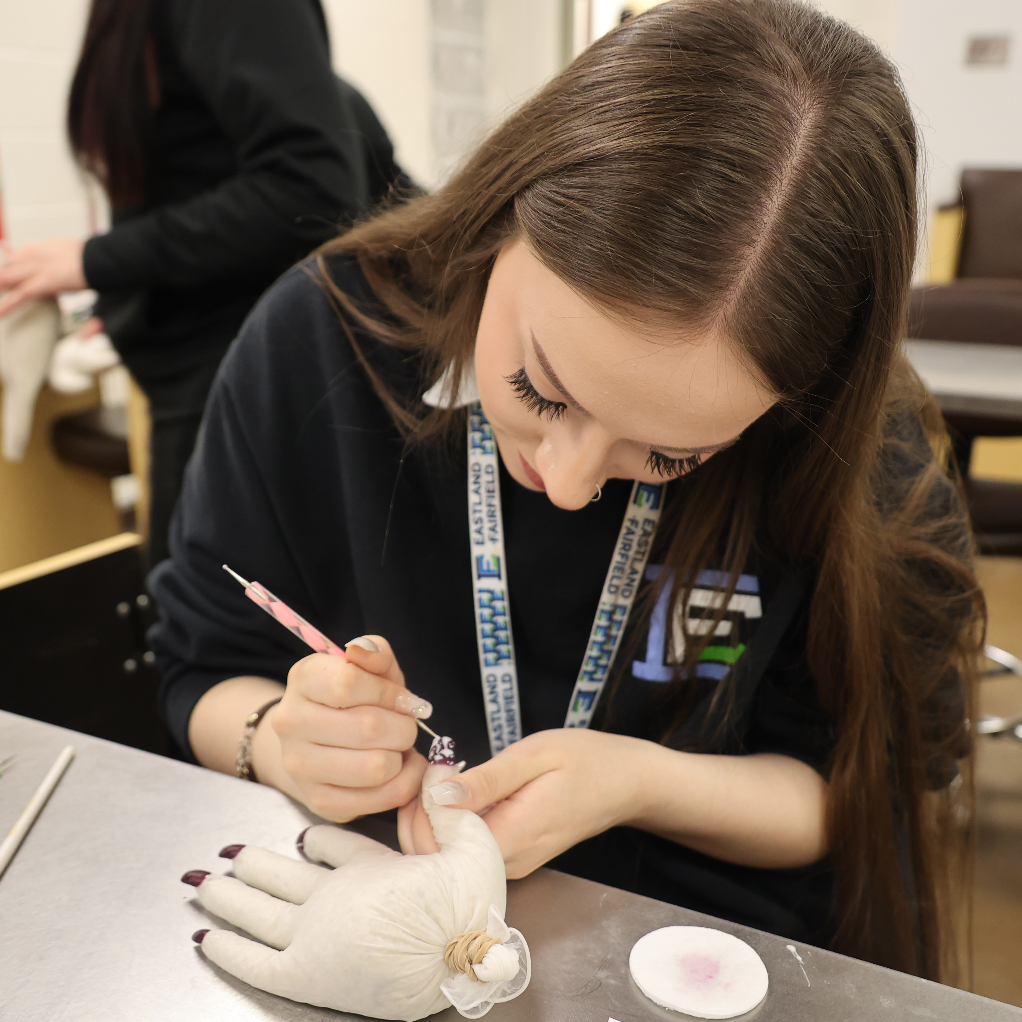 A White, female student is painting nails on a training hand.