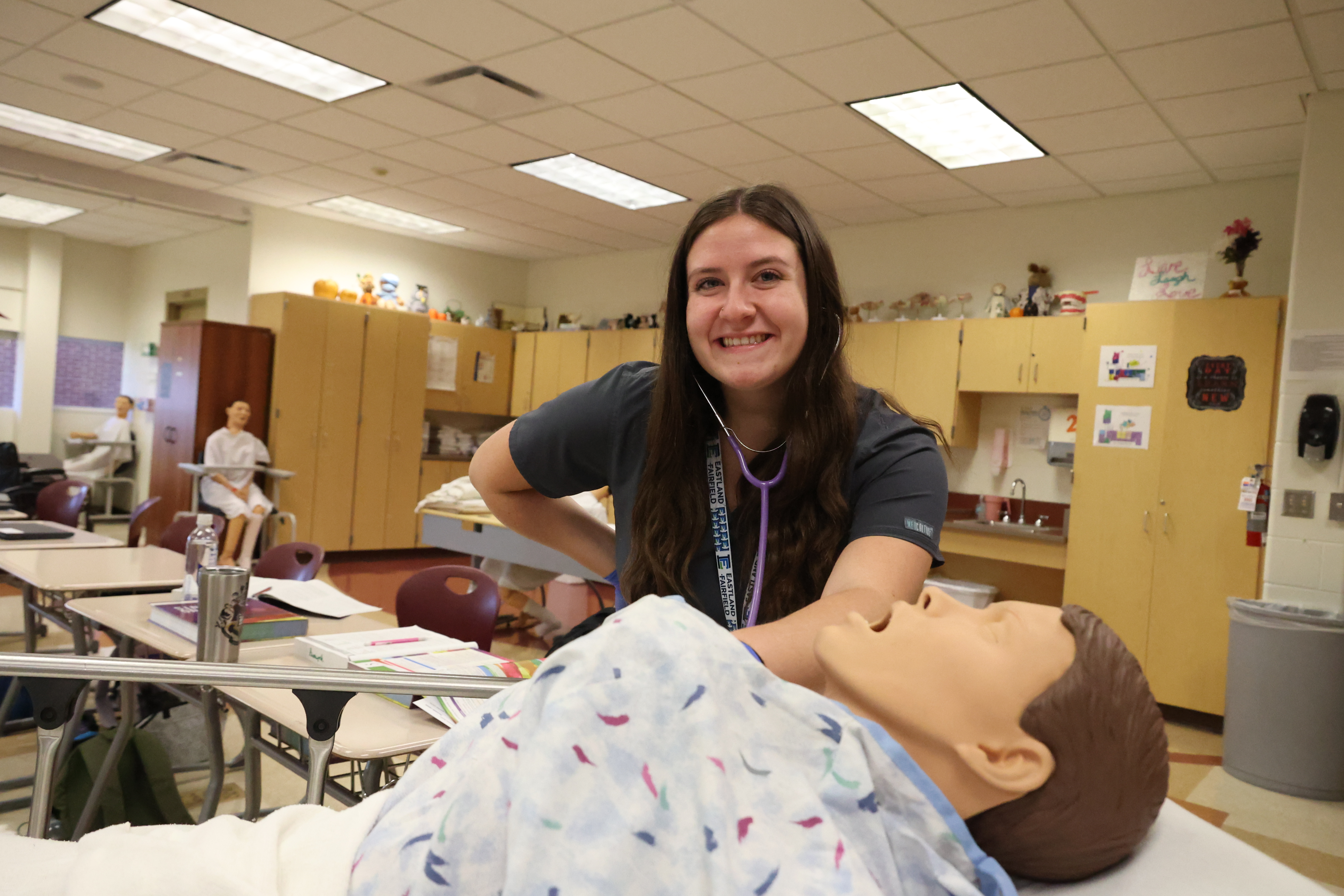 A White, female student measures the heartbeat of a mannequin patient.