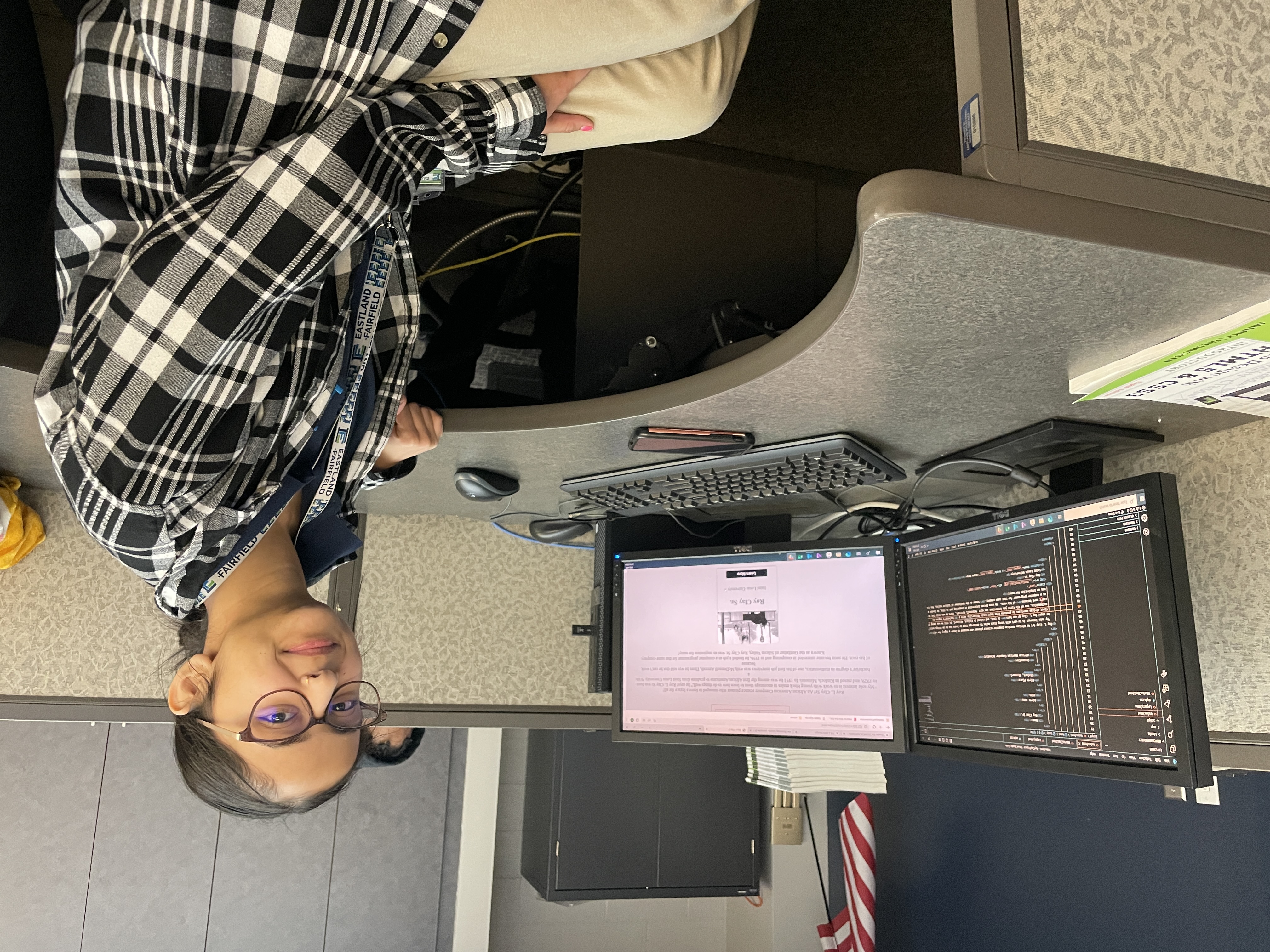 A female student of Indian descent proudly poses at her work station, which displays code for the website she is building from scratch.