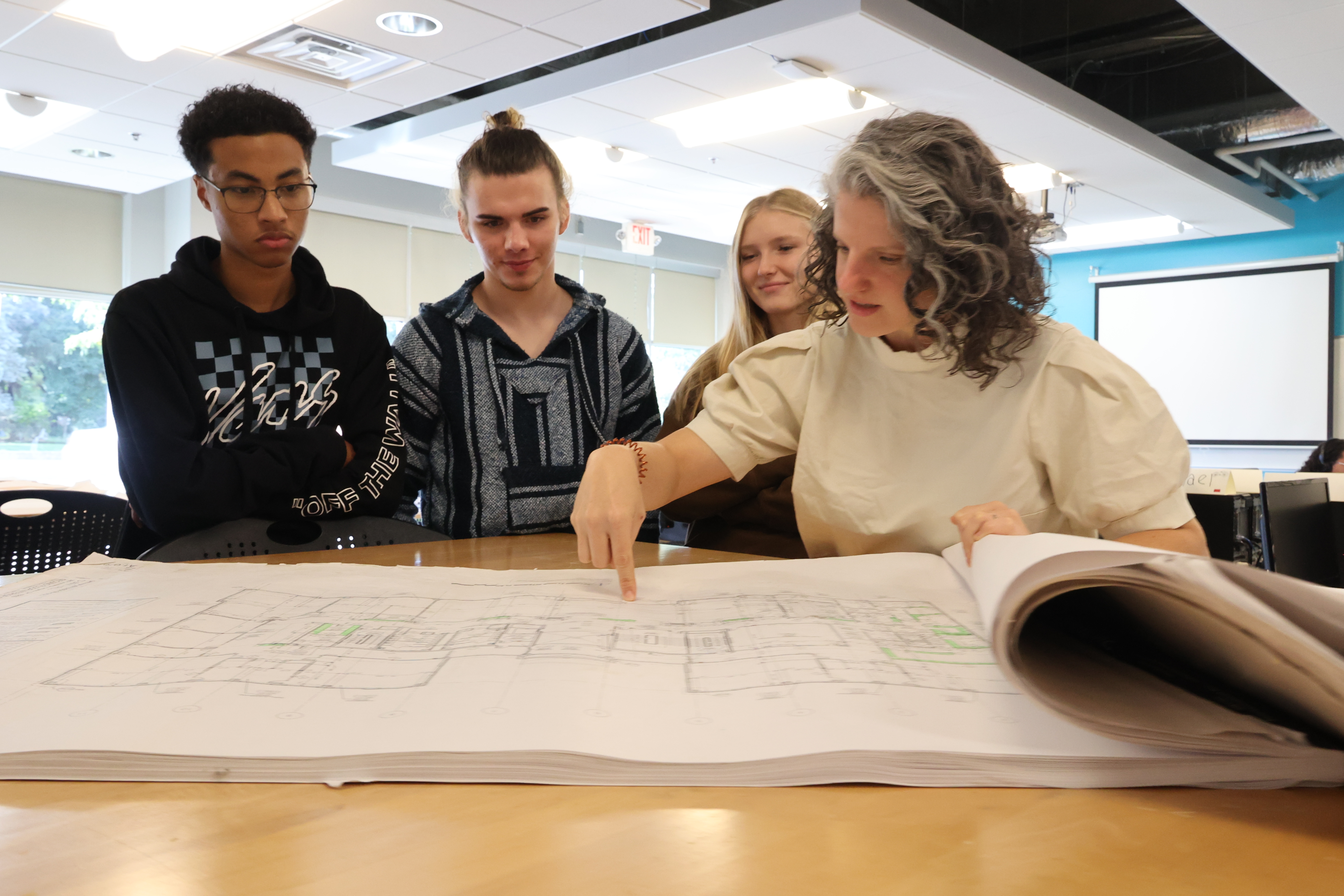 Instructor Amy Smith gathers with three students and is pointing out something on a set of blueprints.
