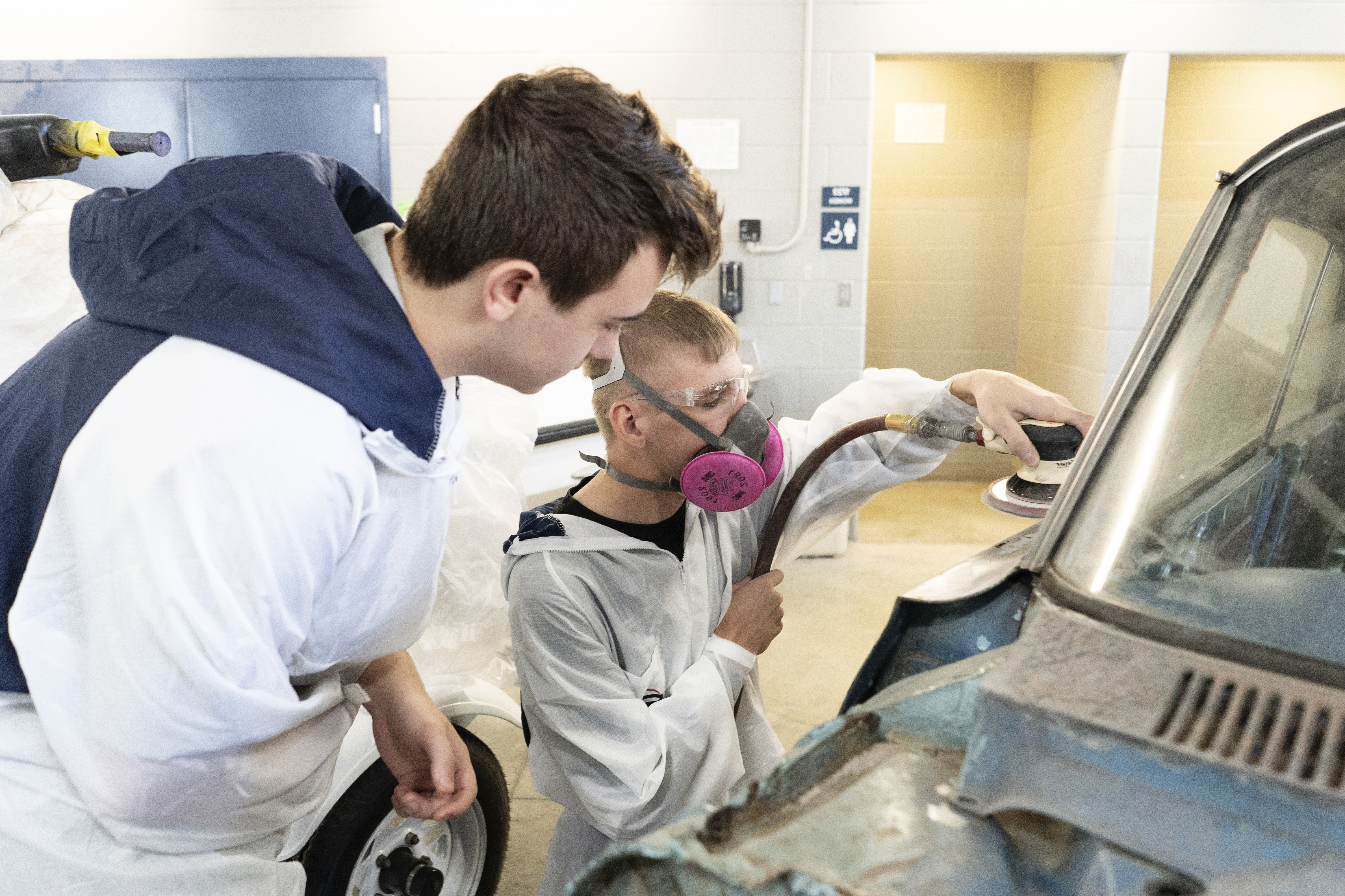 Two white male students are sanding a fender