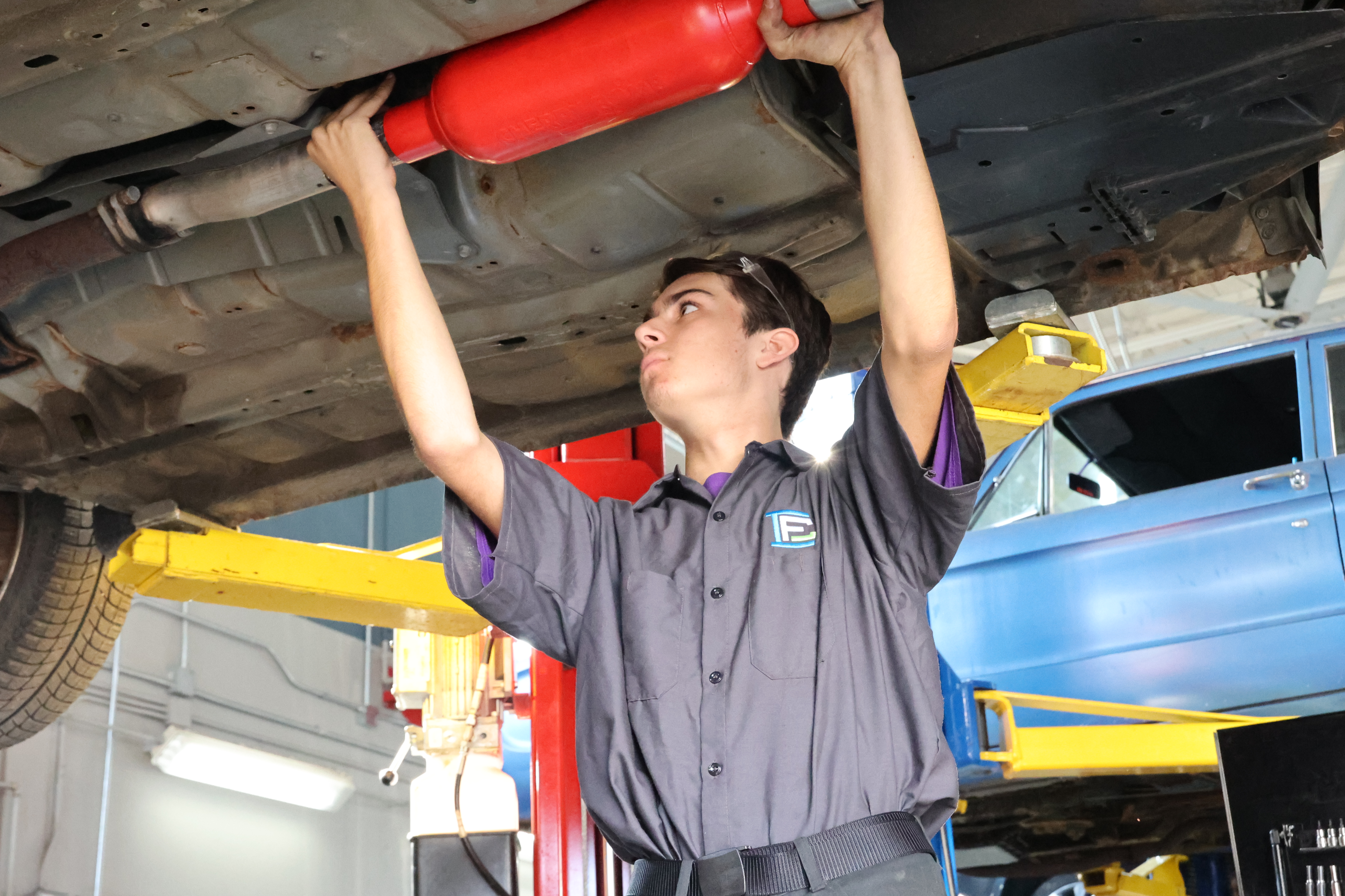 White male student installing a muffler system underneath a car