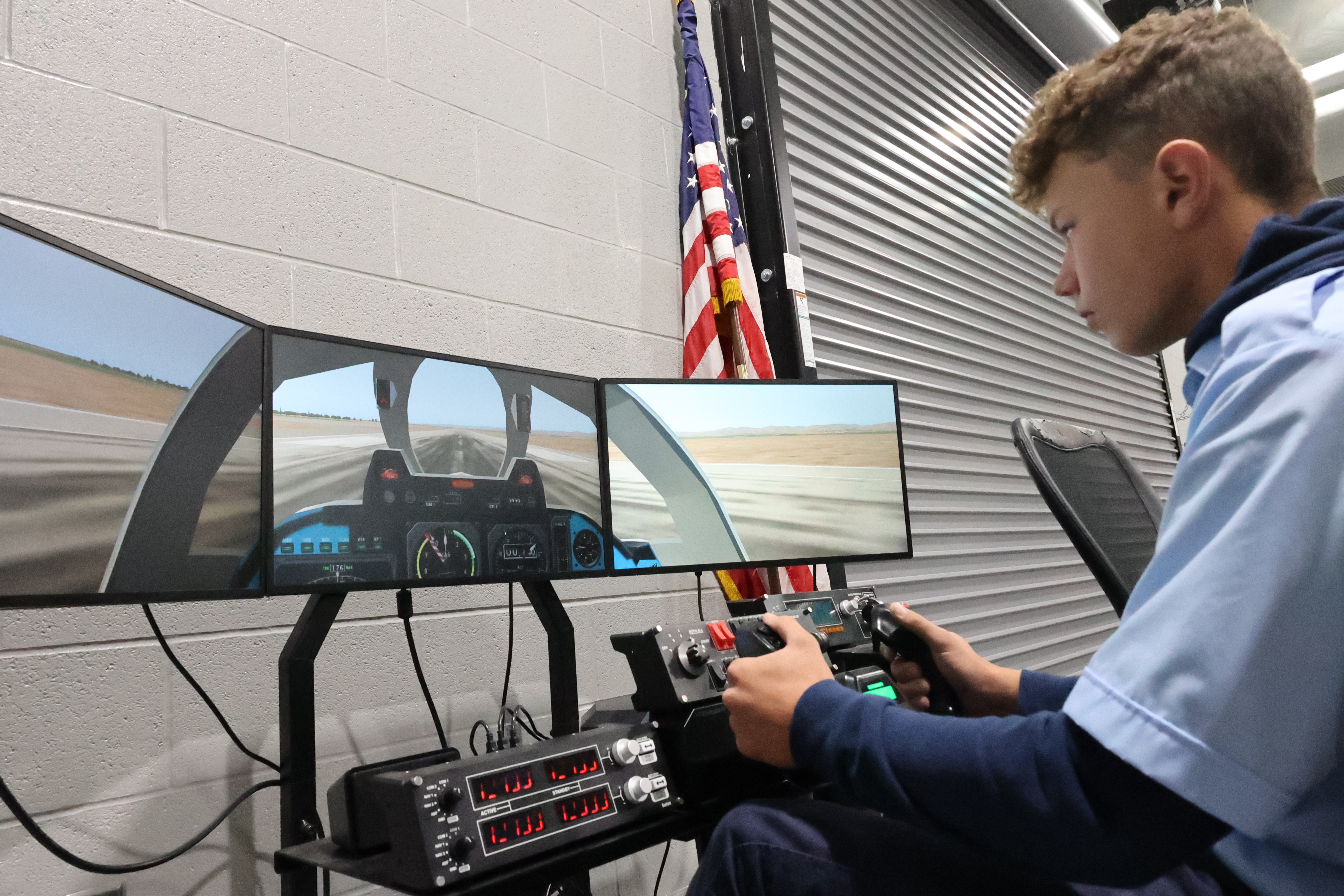 A white male student is seated at a flight simulator and about to take off his digital airplane.