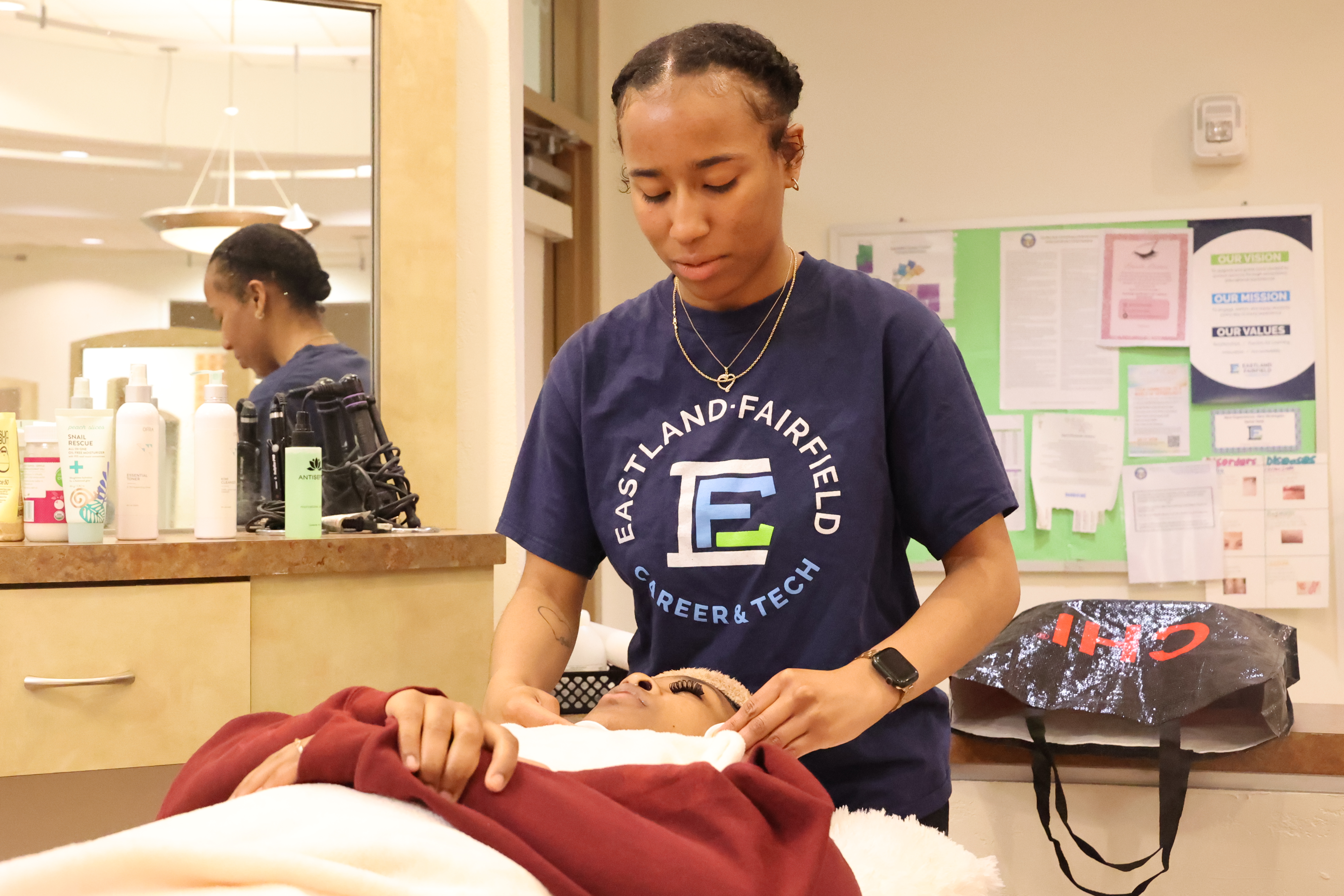 A Black, female student is giving a client a facial.