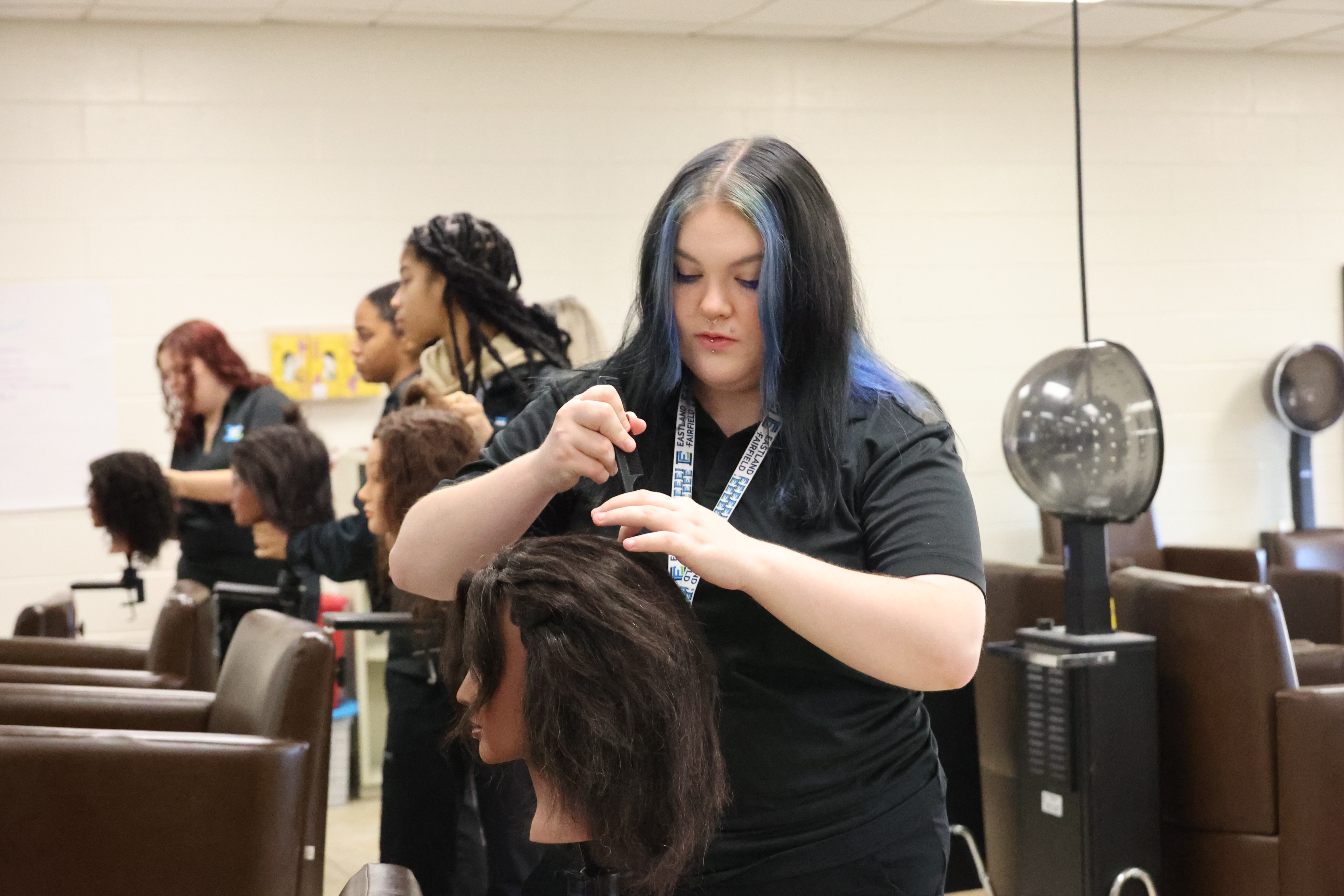 A White, female student is combing out the hair on a mannequin.