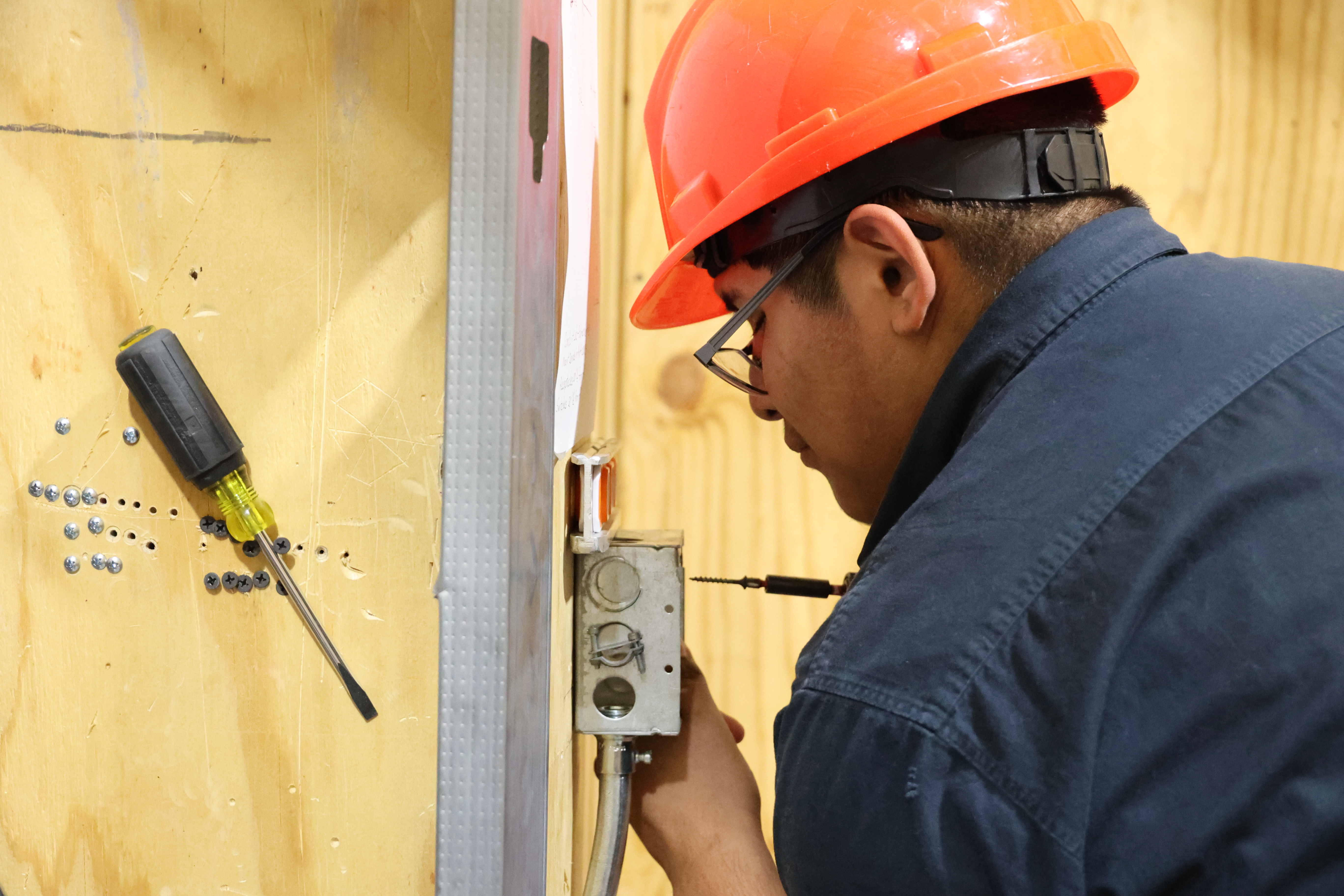 A Hispanic male student lines up a screw before using a hand drill to screw it into his workstation wall.