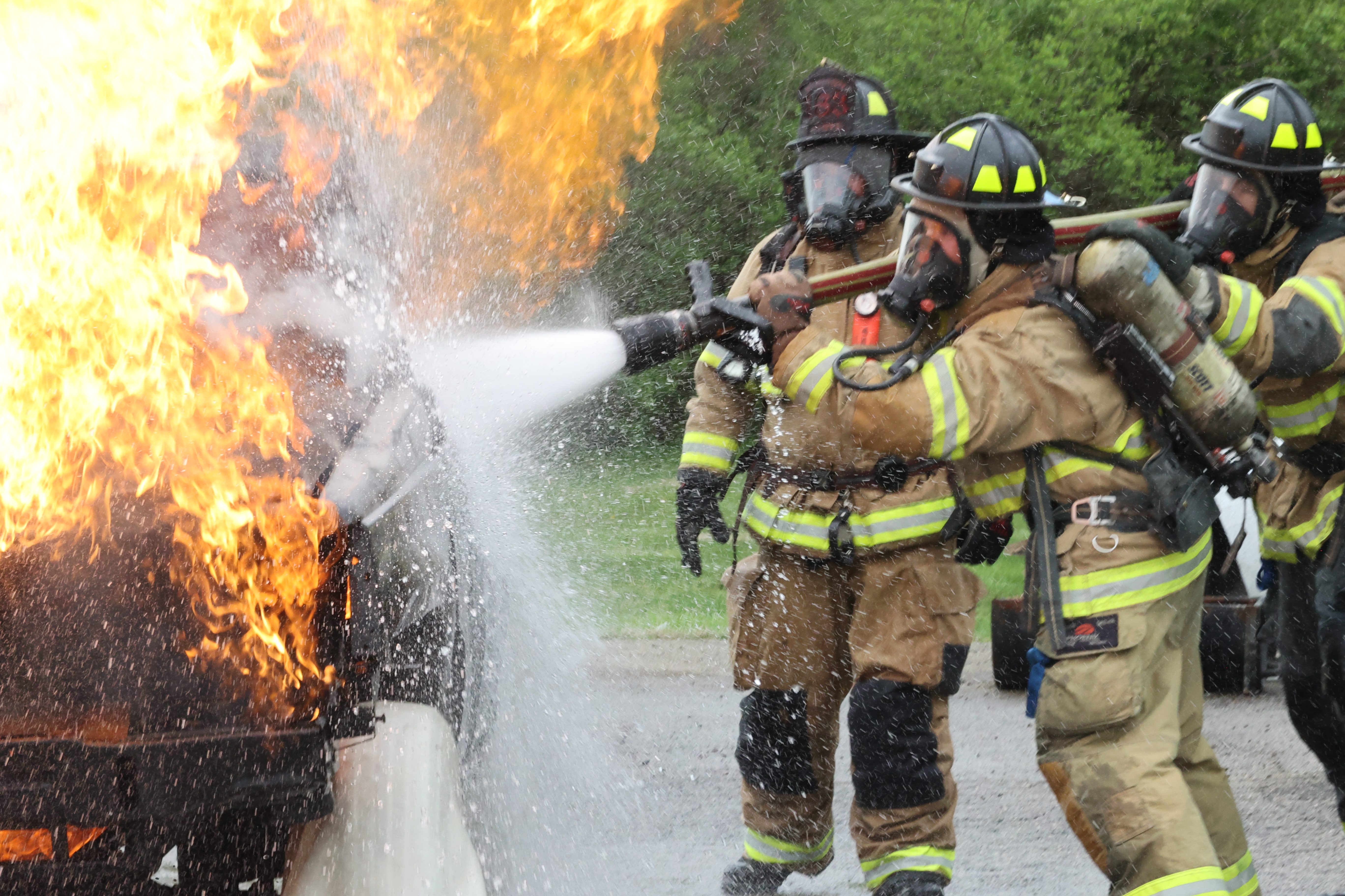 Firefighting students hold a hose spraying water on a burning car