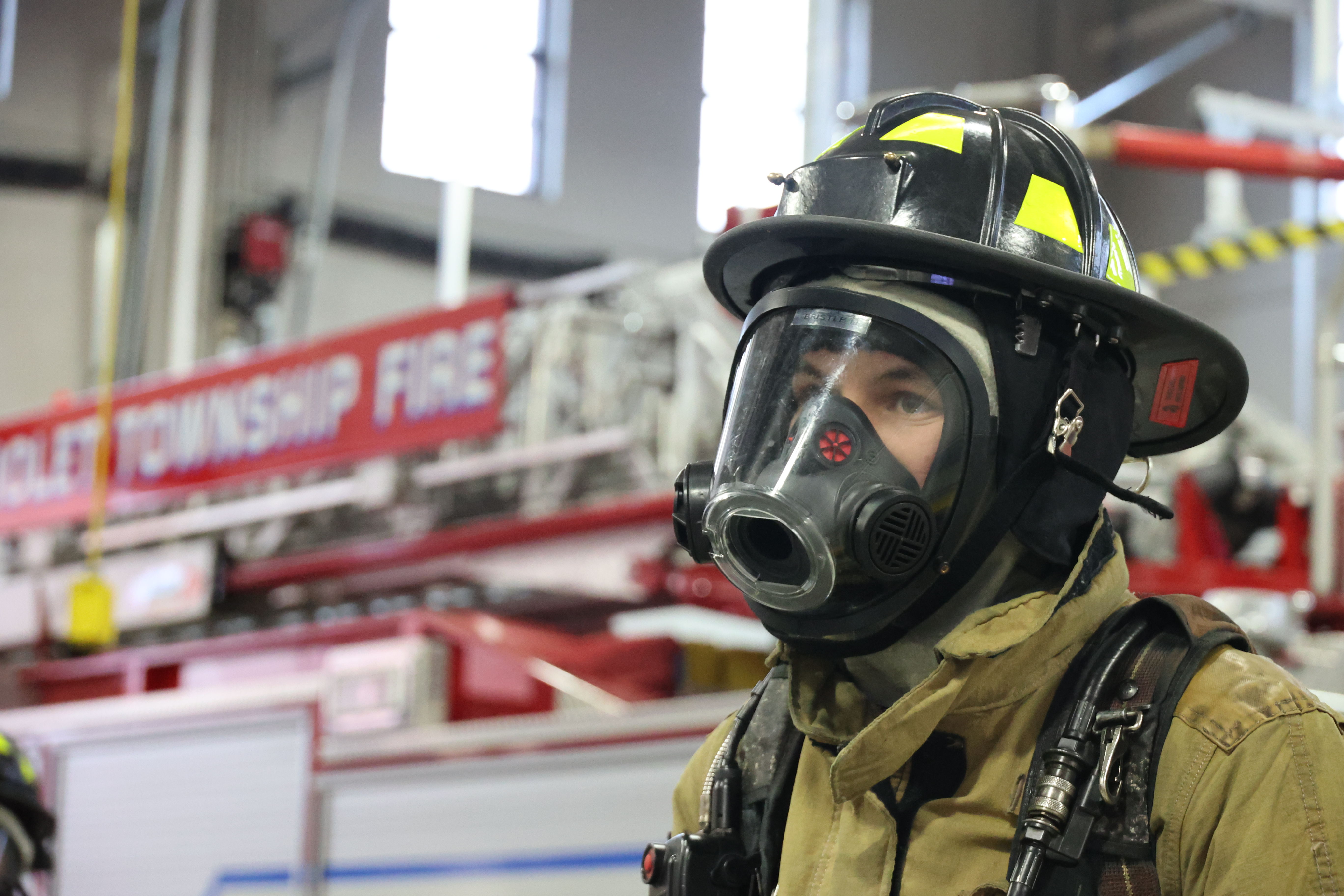 A Firefighting student stands outside of an EMS vehicle in full turnout gear.
