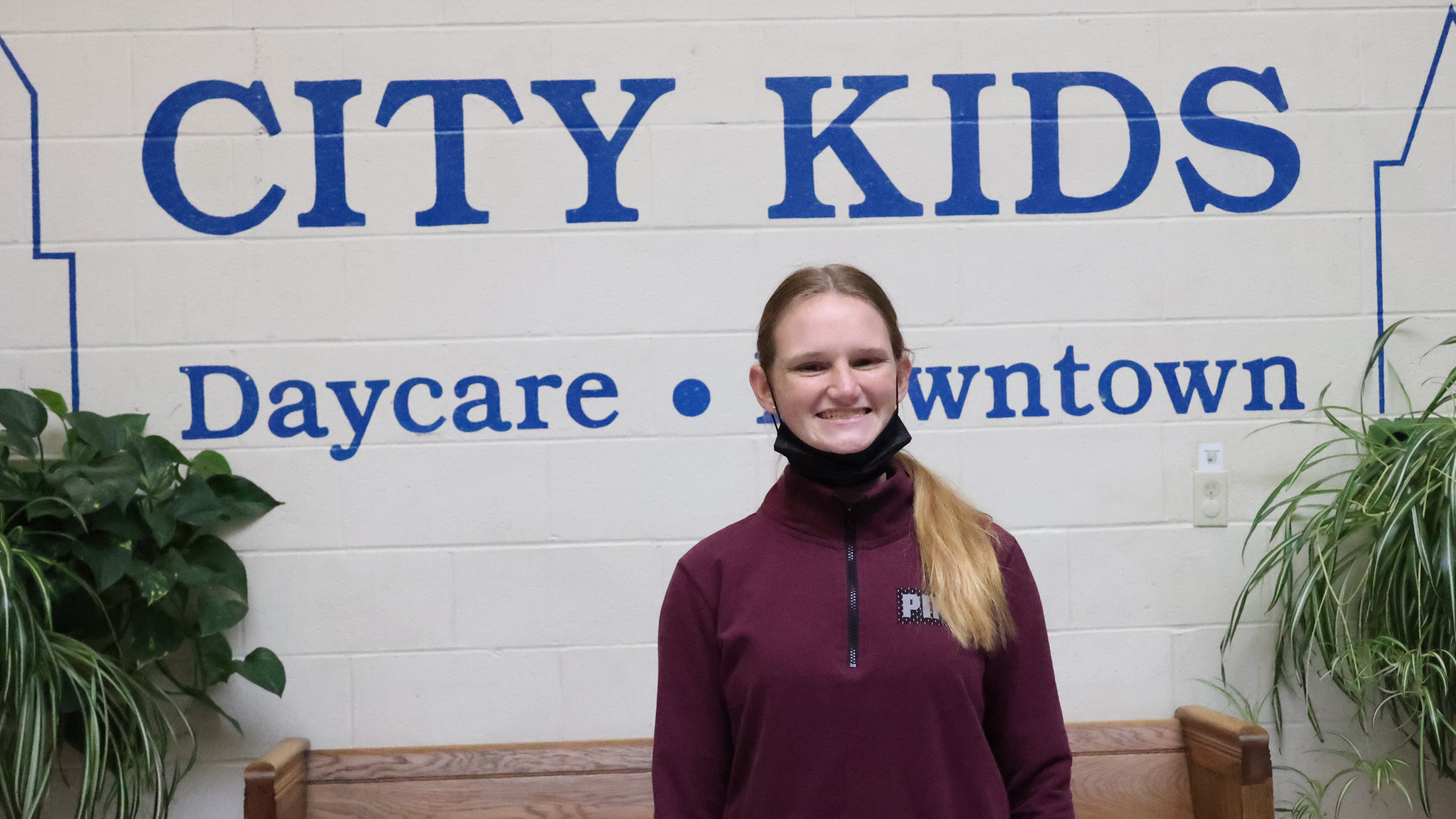 A white female student stands in front of a wall of the daycare she works at