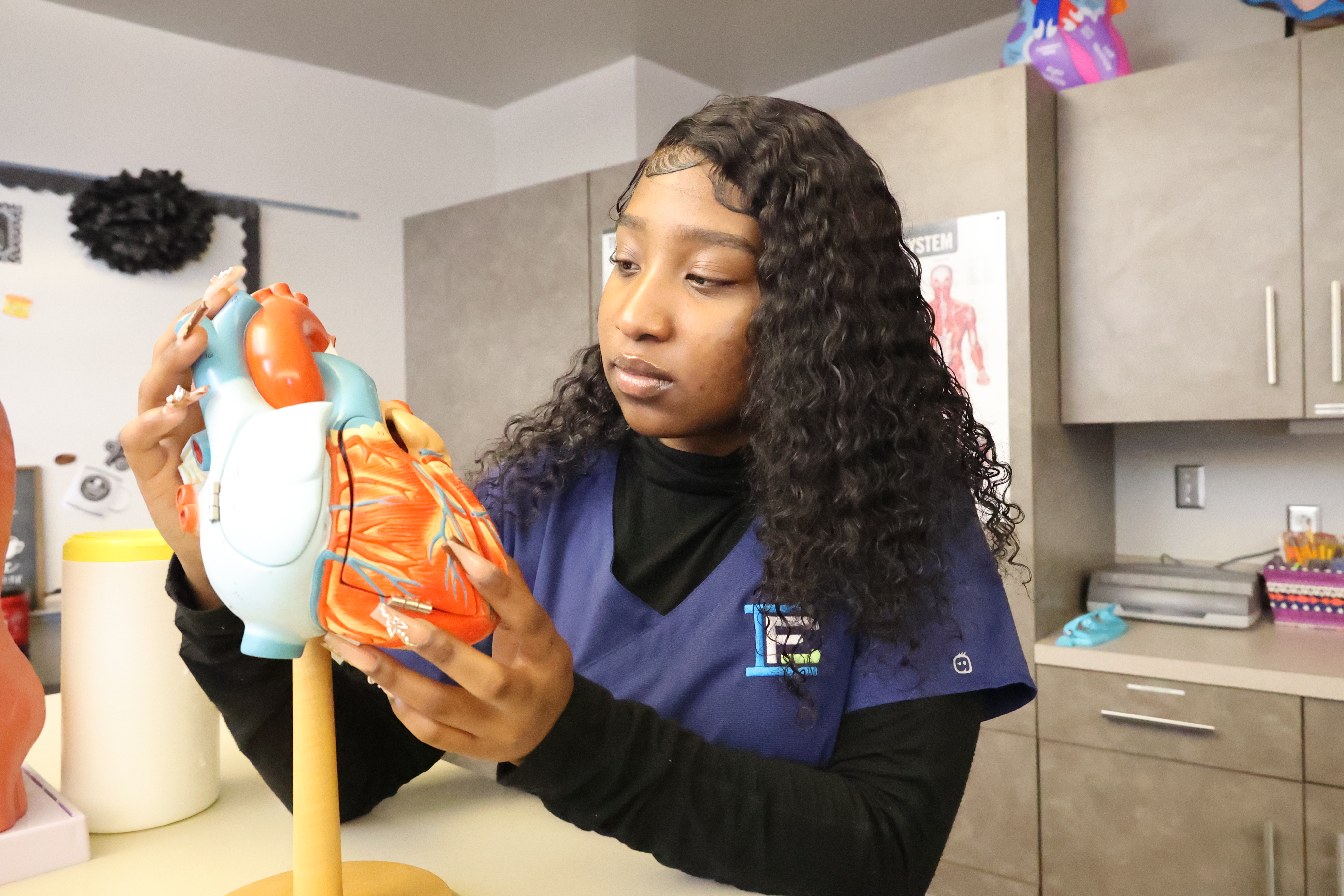 A Black female student is examining a model of the human body.
