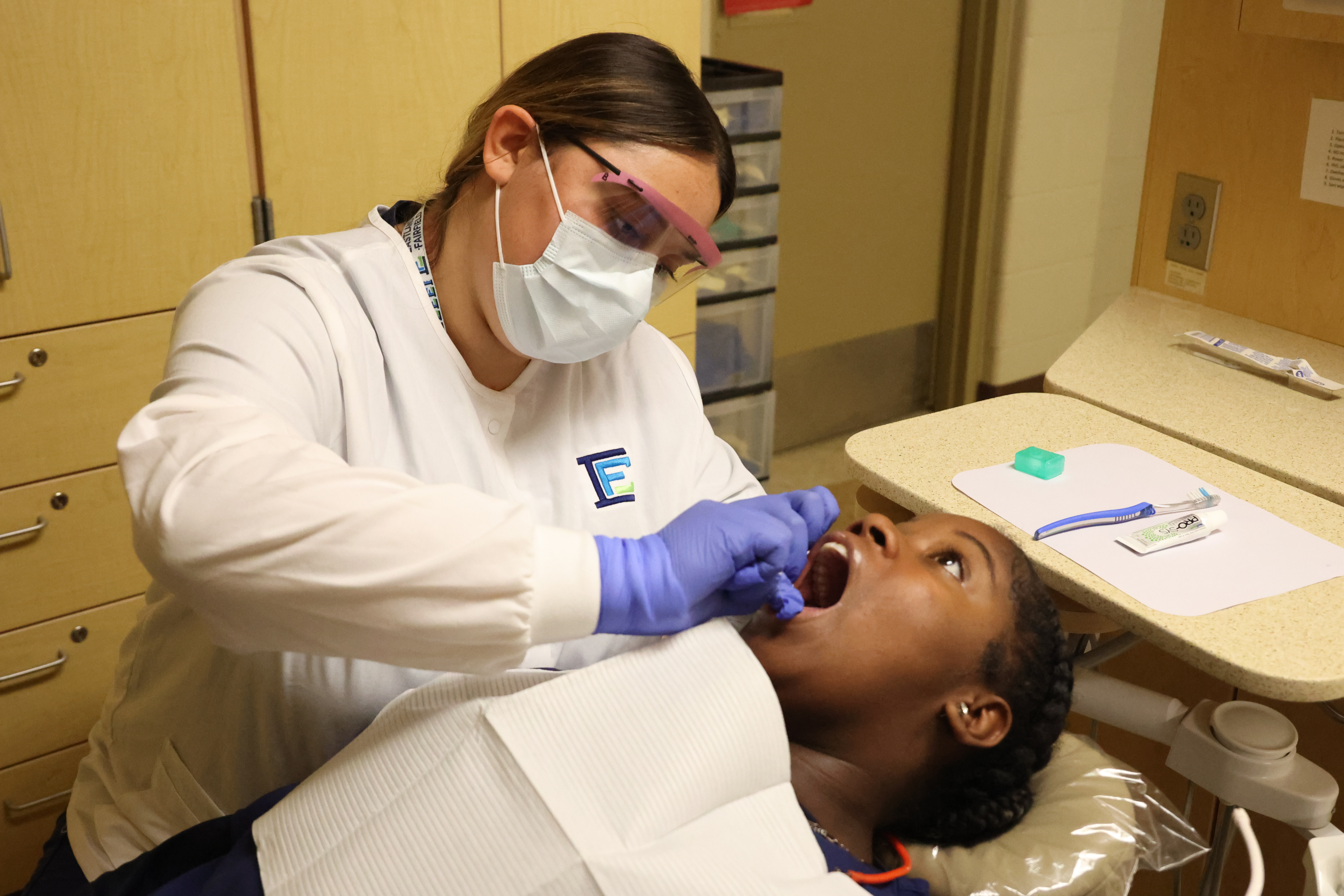 A student in a mask and safety glasses is cleaning another student's teeth in the lab.