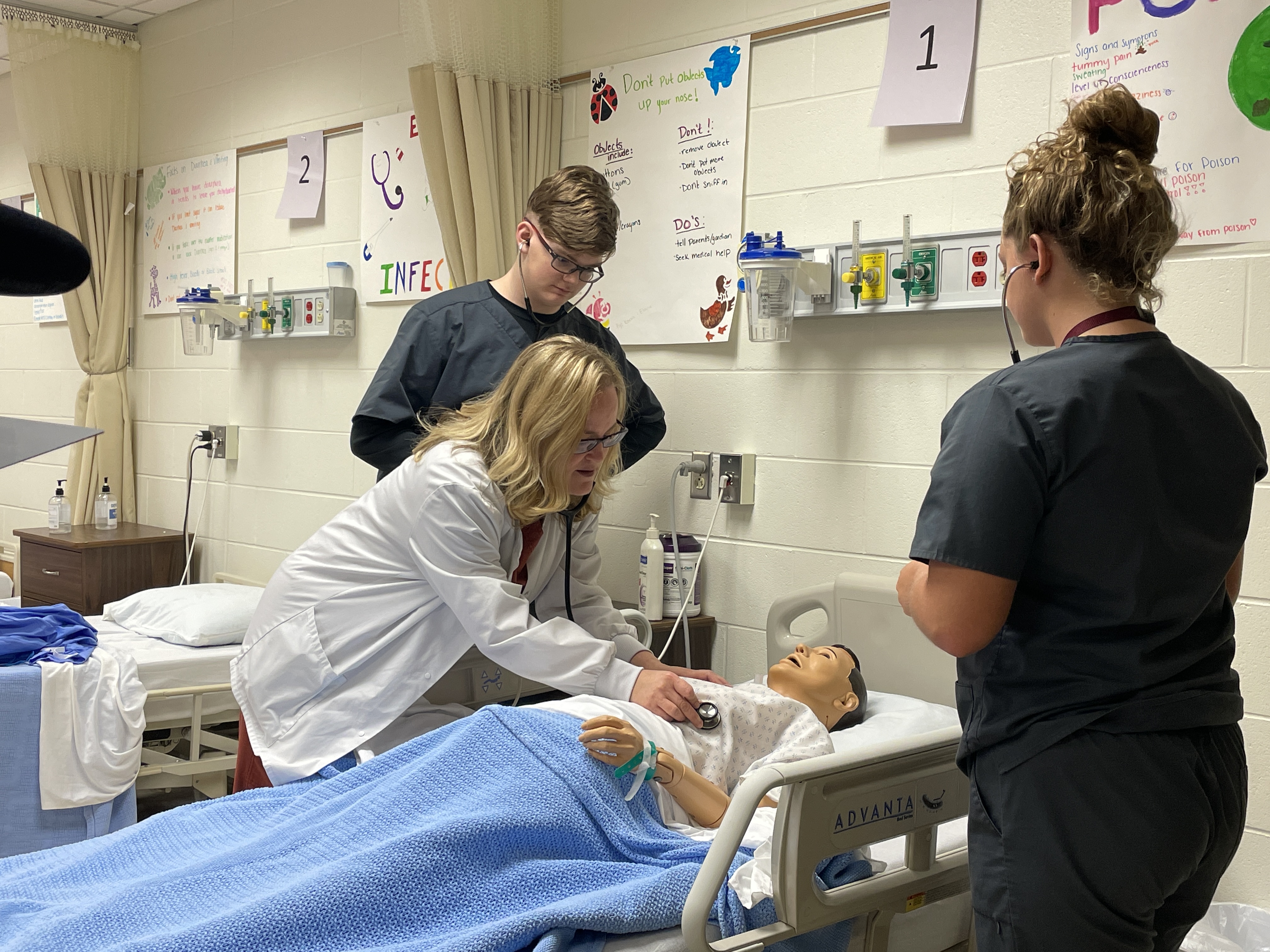 Two students are observing the instructor take vitals with her stethoscope.