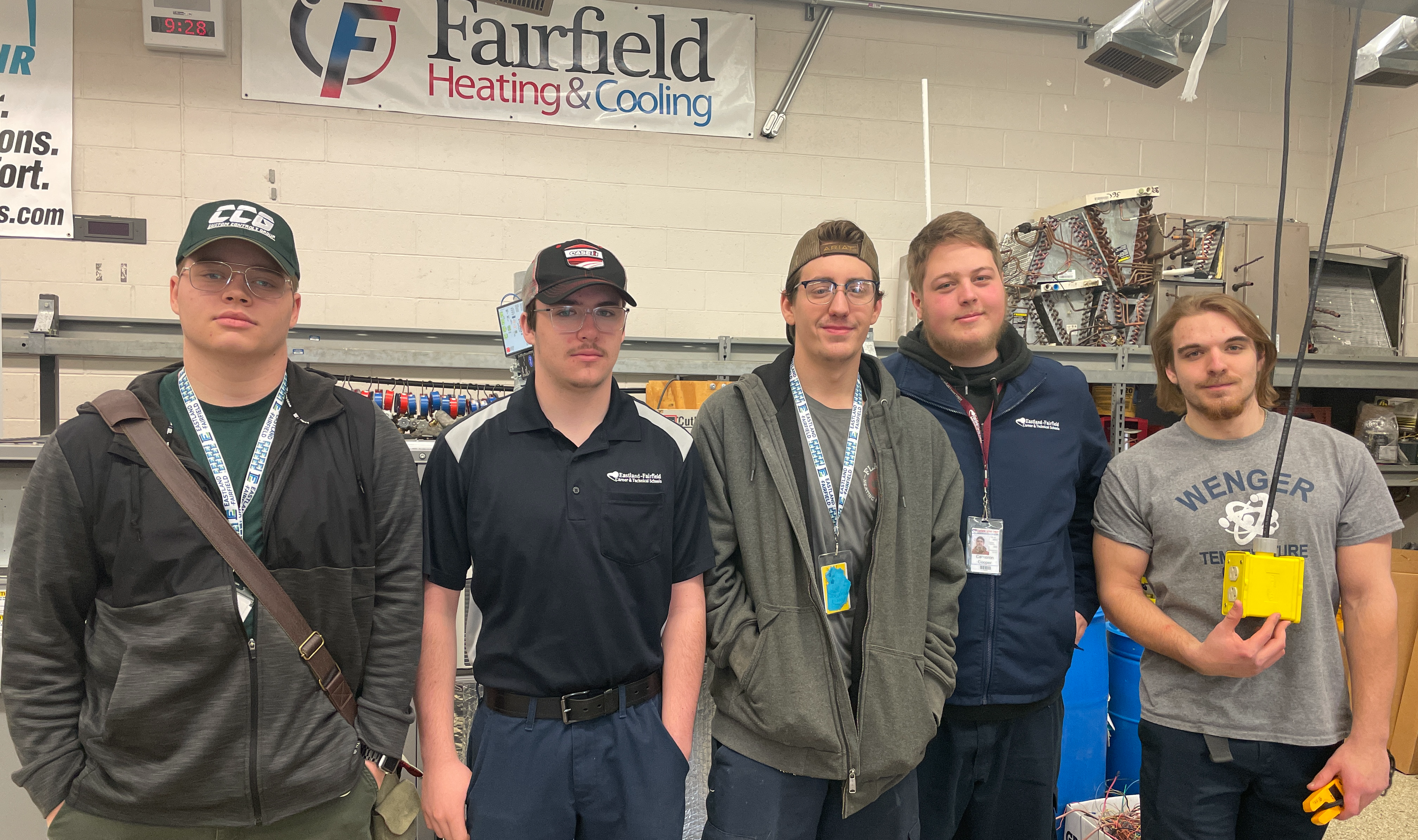 A group of four students that are engaged in WBL experiences gathers for a group photo in their HVAC lab.