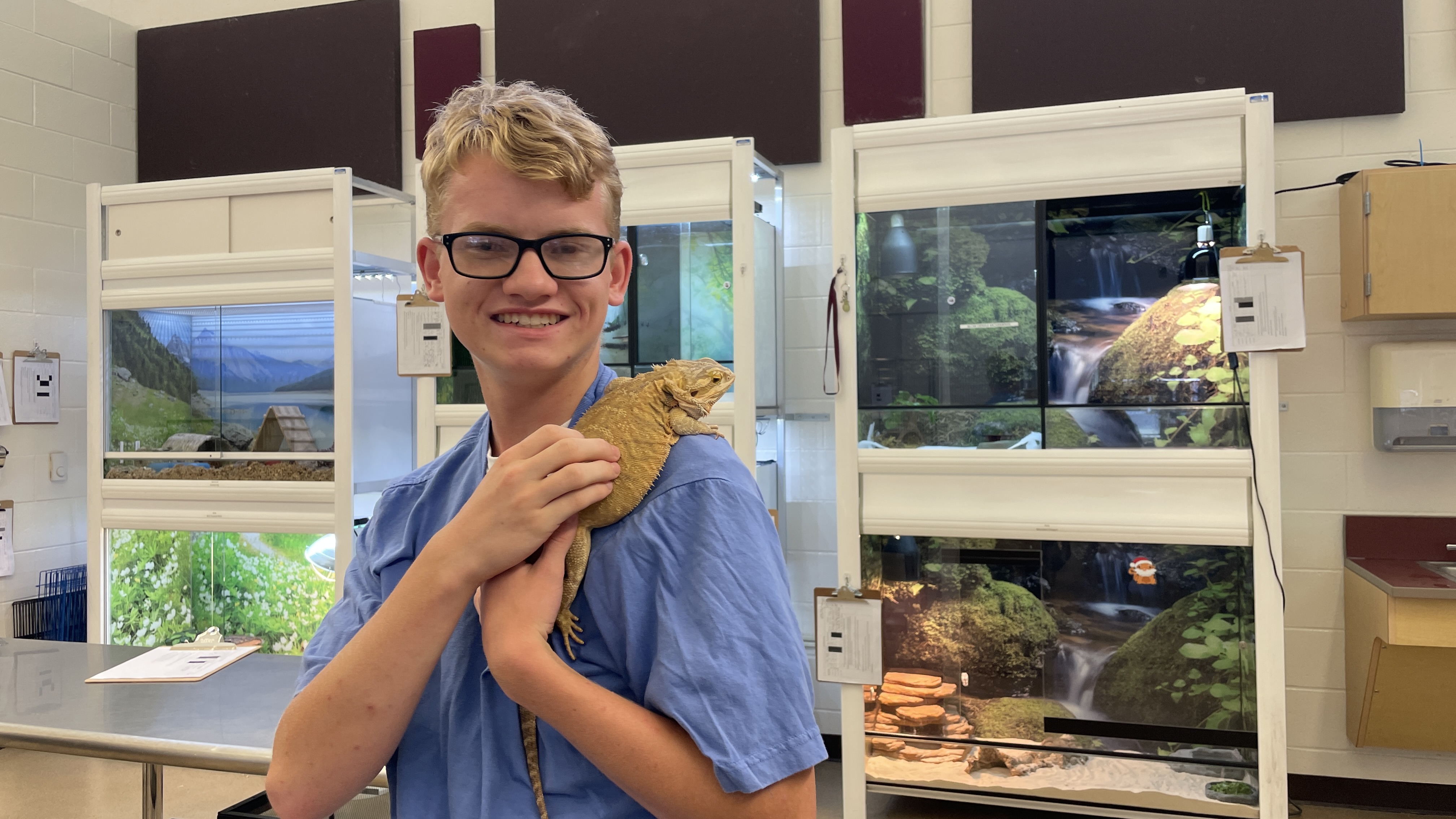 A White, male student lets a reptilian animal rest on his shoulder.
