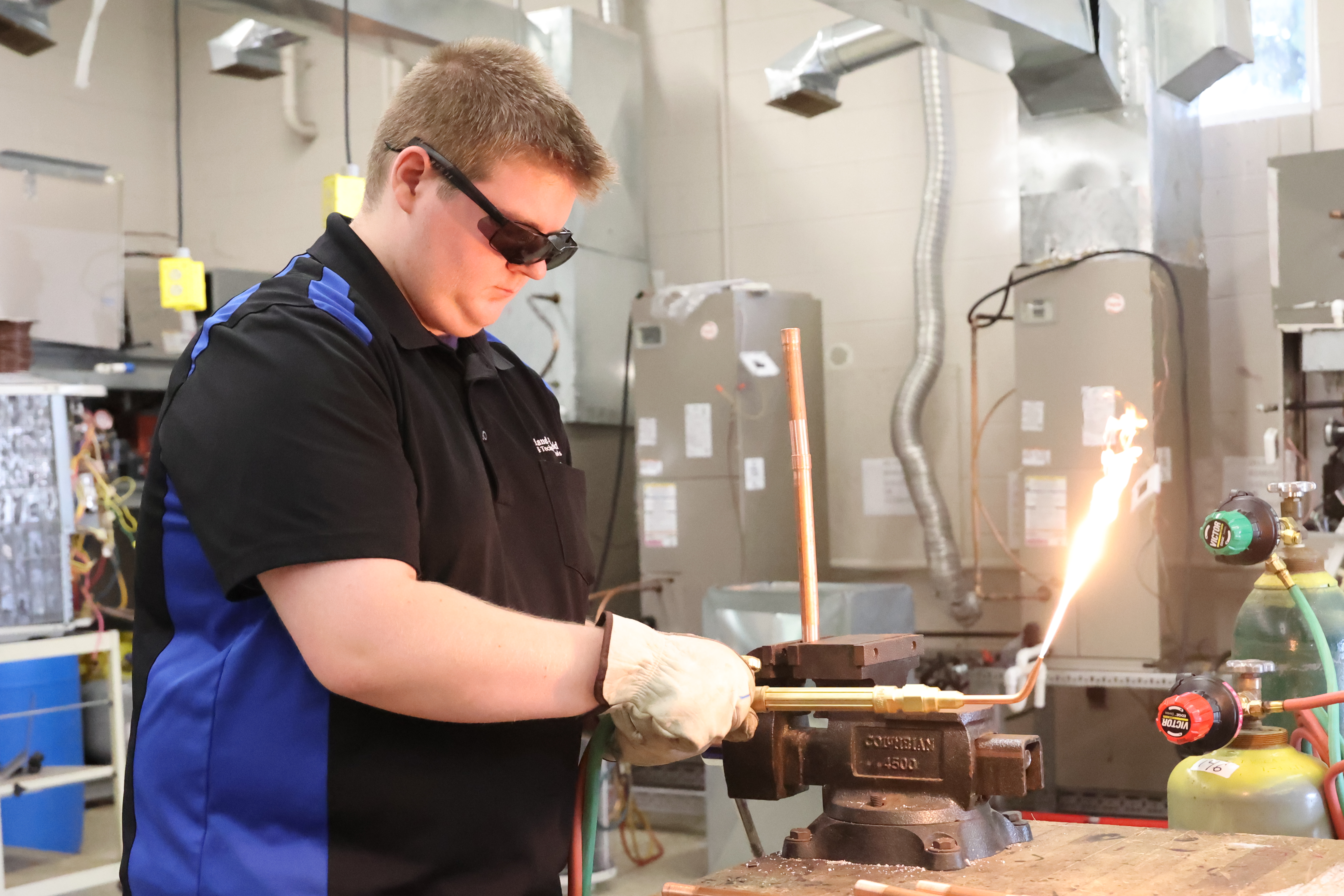A White male student ignites a flame on his torch before getting ready to weld.