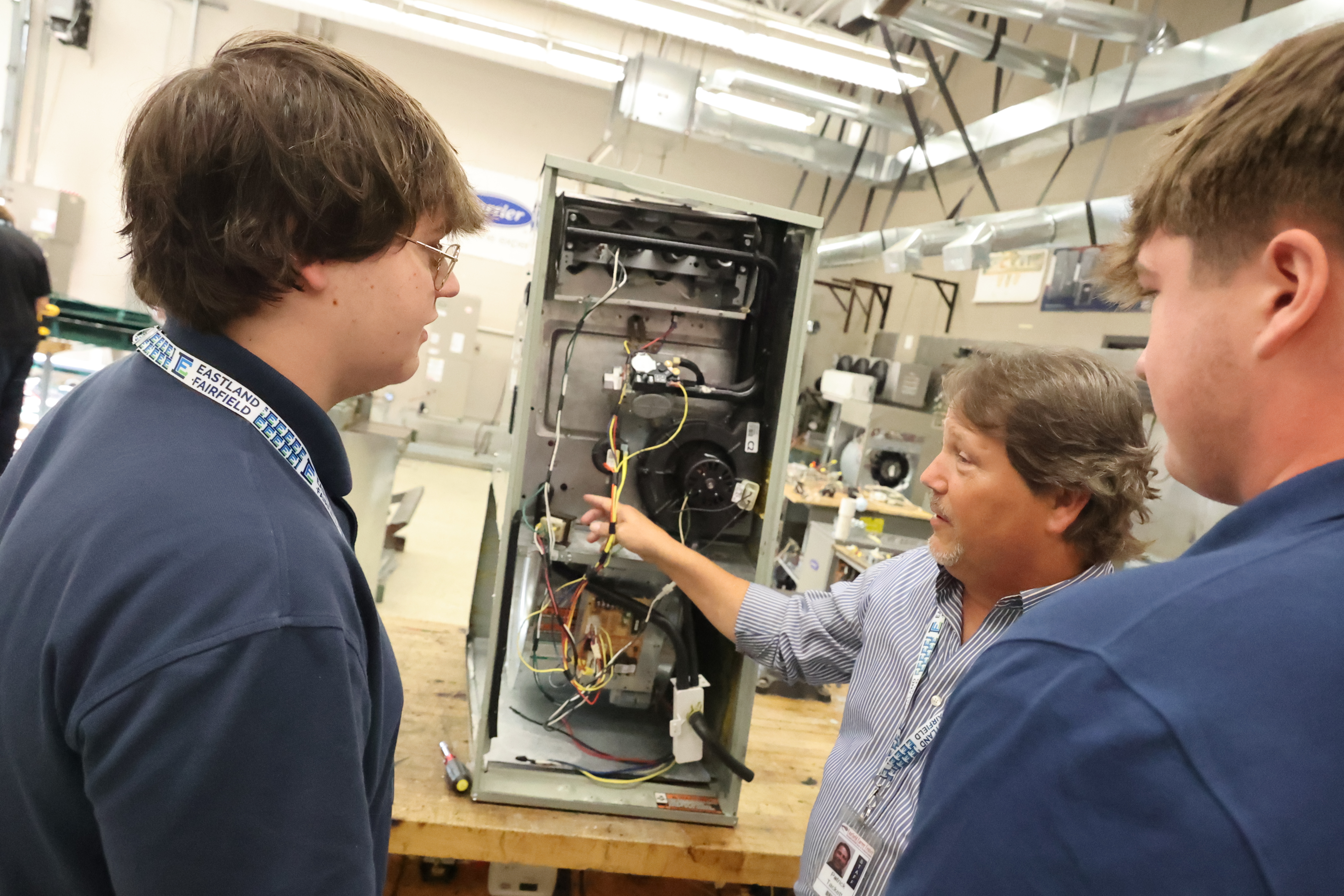 The HVAC instructor reviews the internal parts of a piece of equipment with two students.