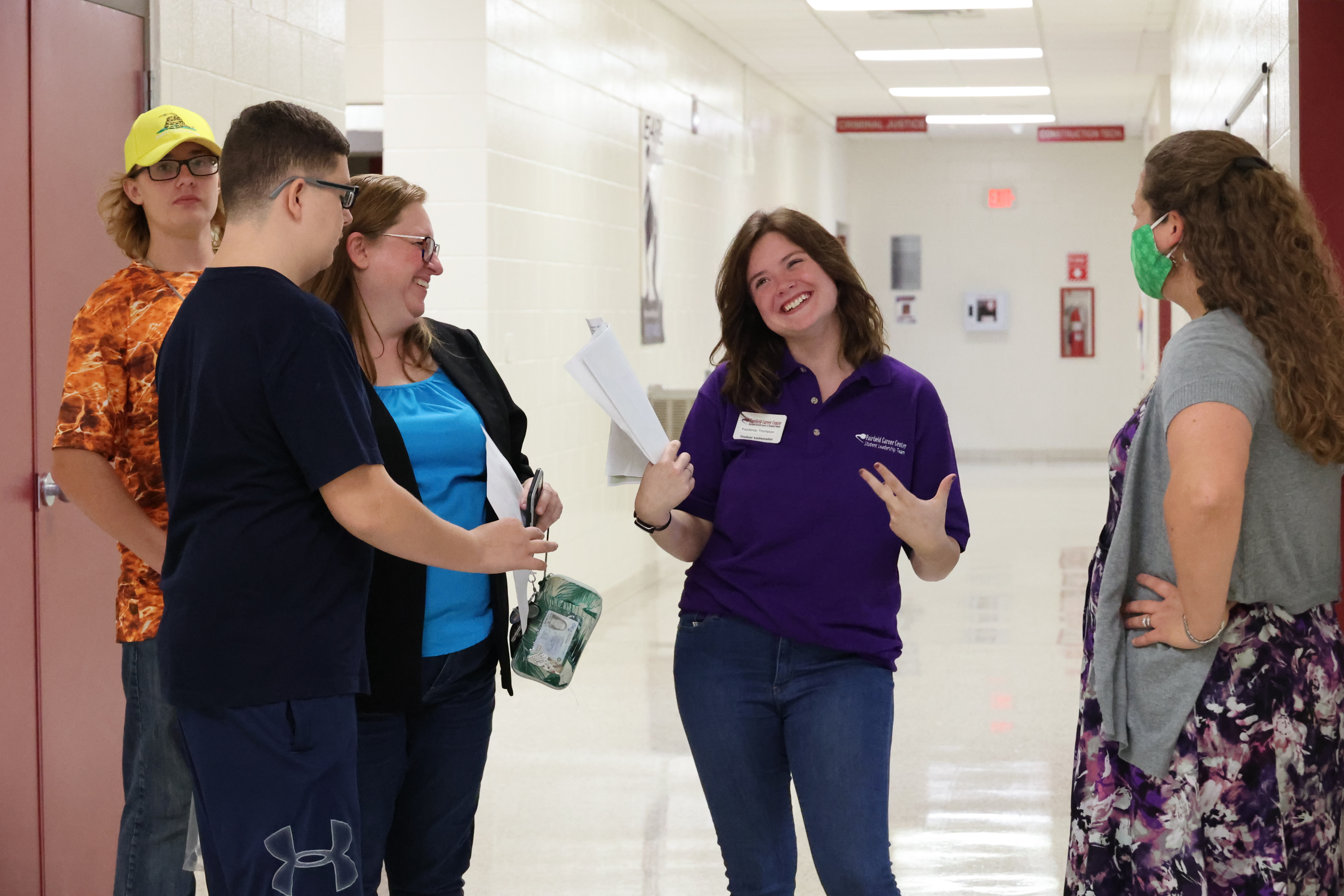 A female student jokes and smiles with a new family in the FCC hallway